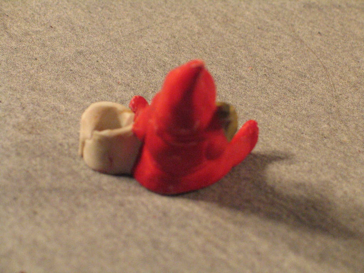 Nisse som sit og spelar trekkbasun. Ved sida av har han ei bøtte som det kan settast juletrelys i. Nissen har langt skjegg og hue med spiss.