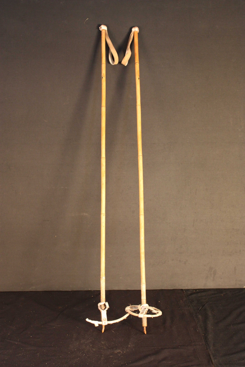 Bambusstavar med skinnreimer som handtak. Skinnreimene er kvite og festa til bambusstavane med ei nagle. På bambusstavane er det spor etter klistermerker med ukjend motiv, men med påskrift "Standard" og "Made in Norway". Trinser av bambus og lær. 