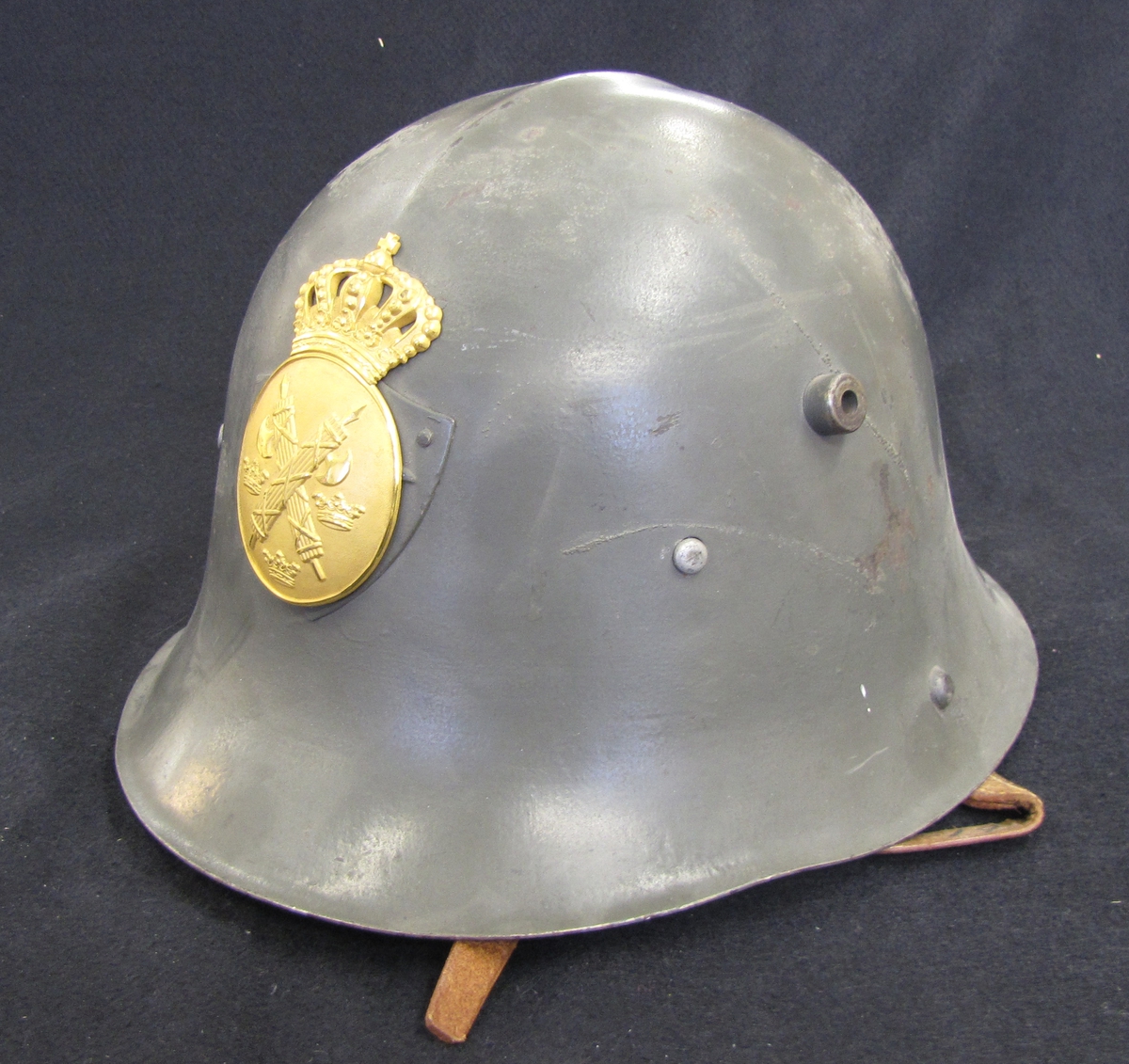 Stålhjälm för polisman (modell 1941). Polisemblem med krona i gulmetall. På emblemet, korslagda fasciner och tre kronor.