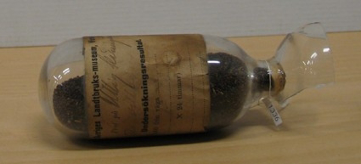 Glasbehållare innehållande fröer av ullig käringtand, gigselärter (Lotus villosus).

Ingår i en frösamling under namn: ''Westra Sveriges Lantbruksmuseum''. Bildat 1880 efter lantbruksmötet i Borås. Samlingen, vilken består av glasbehållare innehållande frön från svenska kulturväxter och träd, uppställdes först på länsresidenset i Vänersborg.

Samlingen kom att bli en av Vänersborgs museums 4 grundsamlingar och uppställdes i museets övre våning vid museets öppnande 1891.

Troligen är glasbehållaren tillverkad vid Reijmyre glasbruk, ligger i Rejmyre, norr om Norrköping.