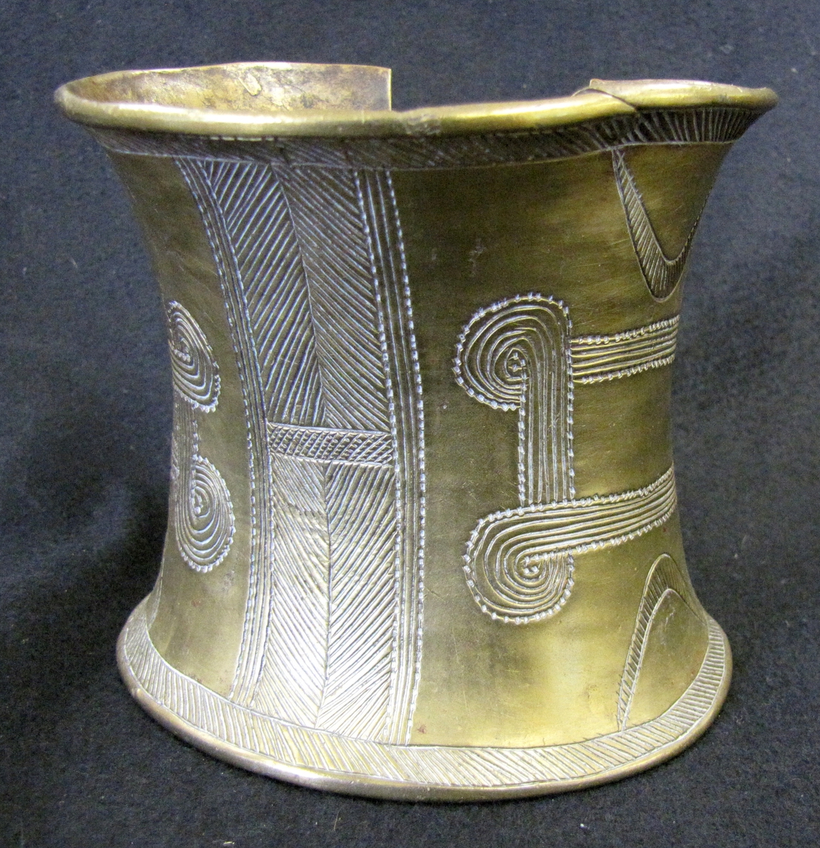 Armband, cylindriskt konkav i formen. Ena sidan av armbandet är öpen. Armbandet är rikt dekorerad med graverade mönster.