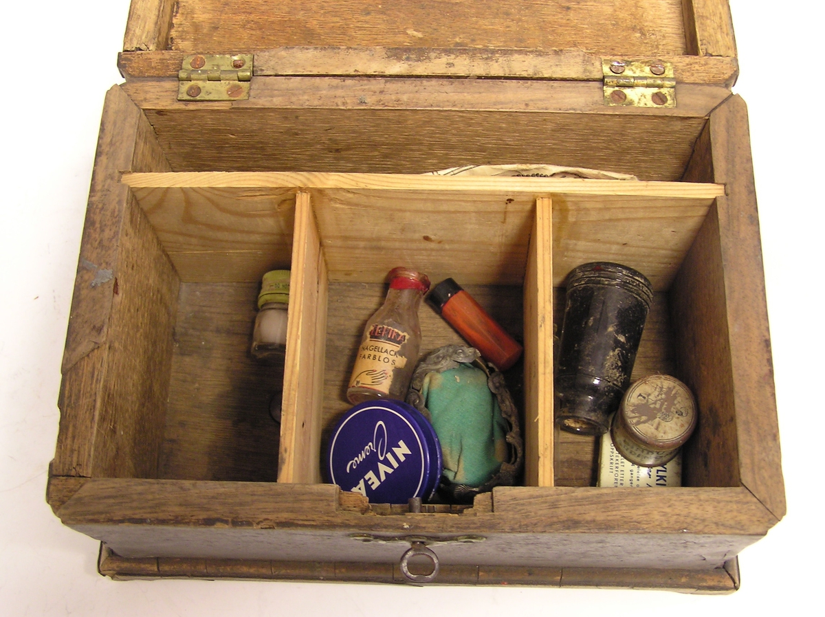 Rektangulær skrin med lokk og nøkkelhull. Liten nøkkel ligger i hullet.  Fotliste. Rommet er inndelt og inneholder små medisinflasker, krem og hodetabletter.
Ligner liten skipskiste.