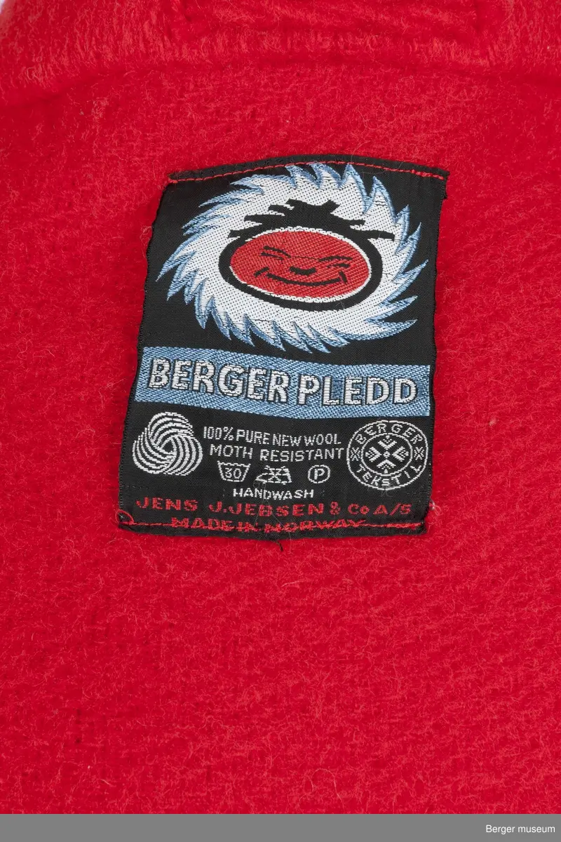 Lang rød kåpe med store røde knapper, krage, lommer og oppbrettede ermer. Det er sydd på skulderputer i skumgummi med silketrekk.
Møllsikret. 