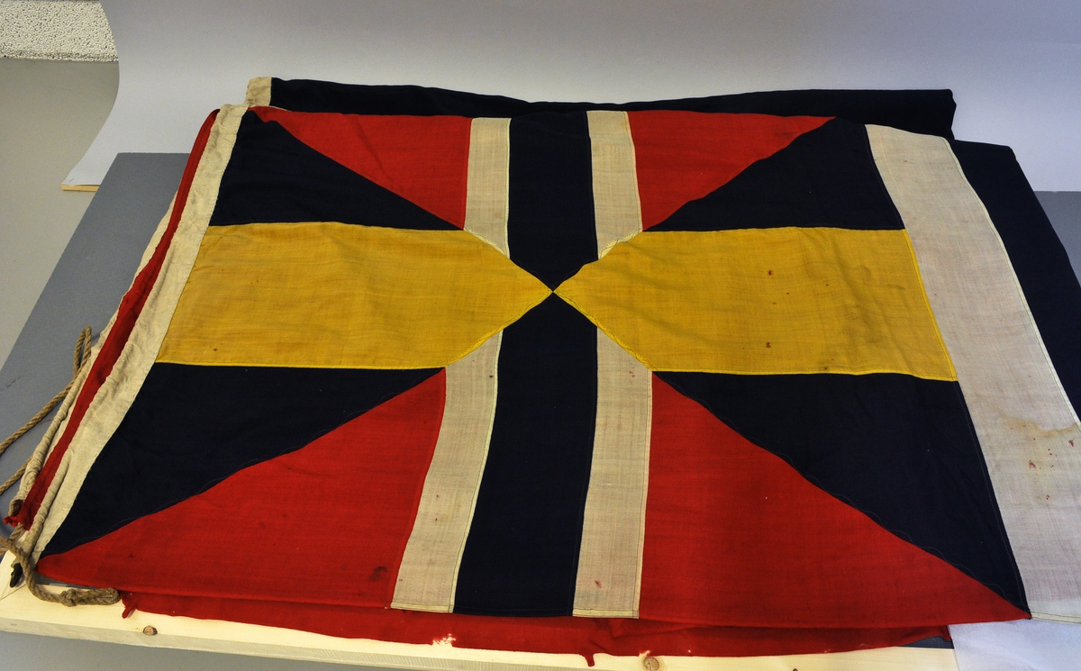 Norsk flagg med unionsmerke ("sildesalat). Unionsmerket er applikert på en rød rute øverst i høyre hjørne.
Det er påmontert  kanalgang(5,5cm) for feste av tau. Inne i kanalgangen er det antakeligvis tau av hamp. I enden av kanalgangen er det montert på en festeanordning av metall.