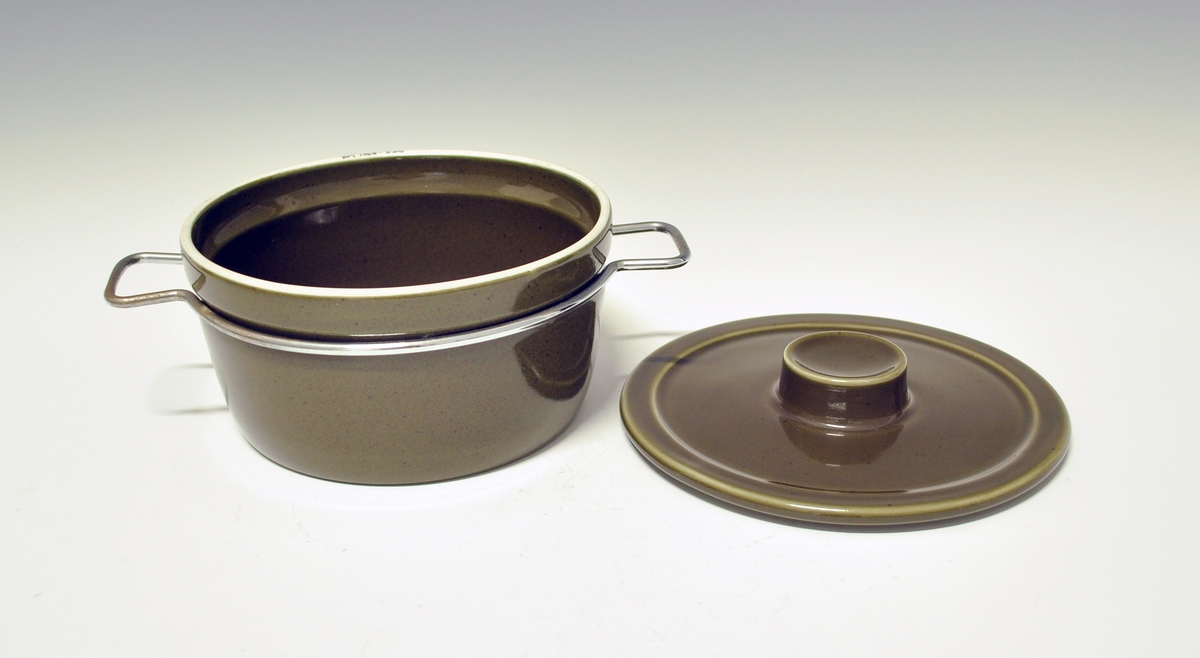 Gryte med lokk av porselen, ildfast gods. Mørkegrønn glasur. Metallhanker.
Modell 2376 Askeladden av Eystein Sandnes, i produksjon fra 1964.