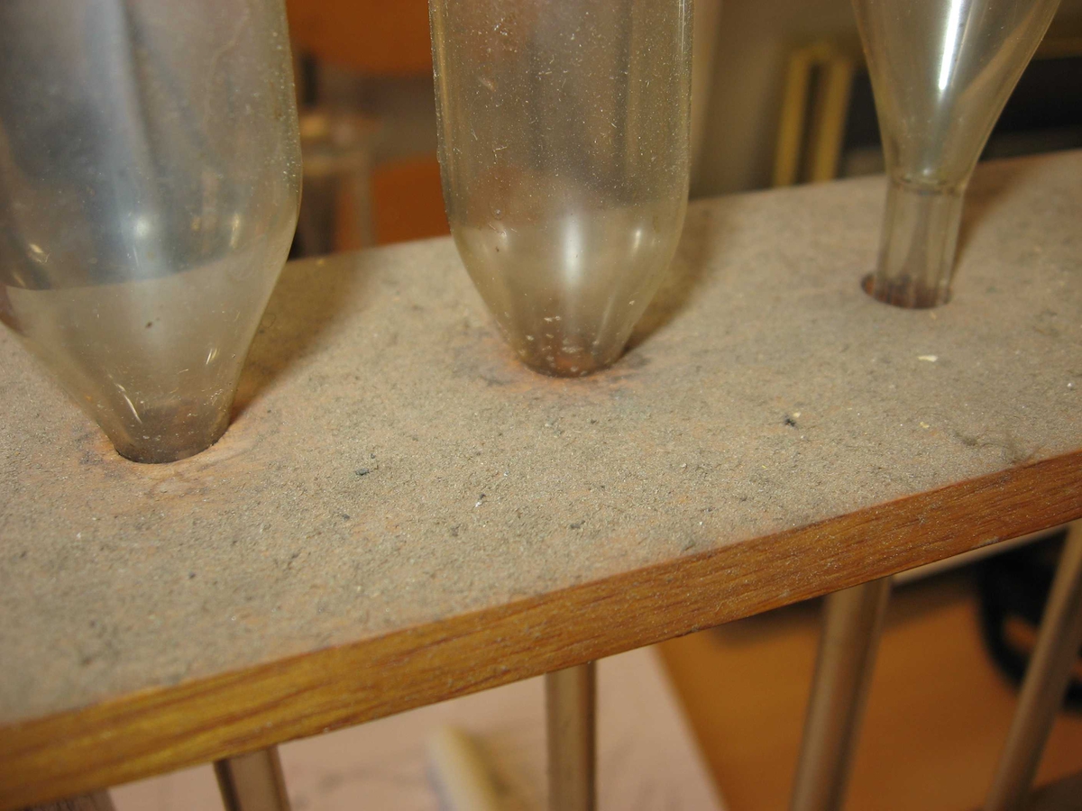 9 glassrør, med kul (kolbe) på midten og pipette-hull i den ene enden. Det er plass til 2 rør til i trestativet.