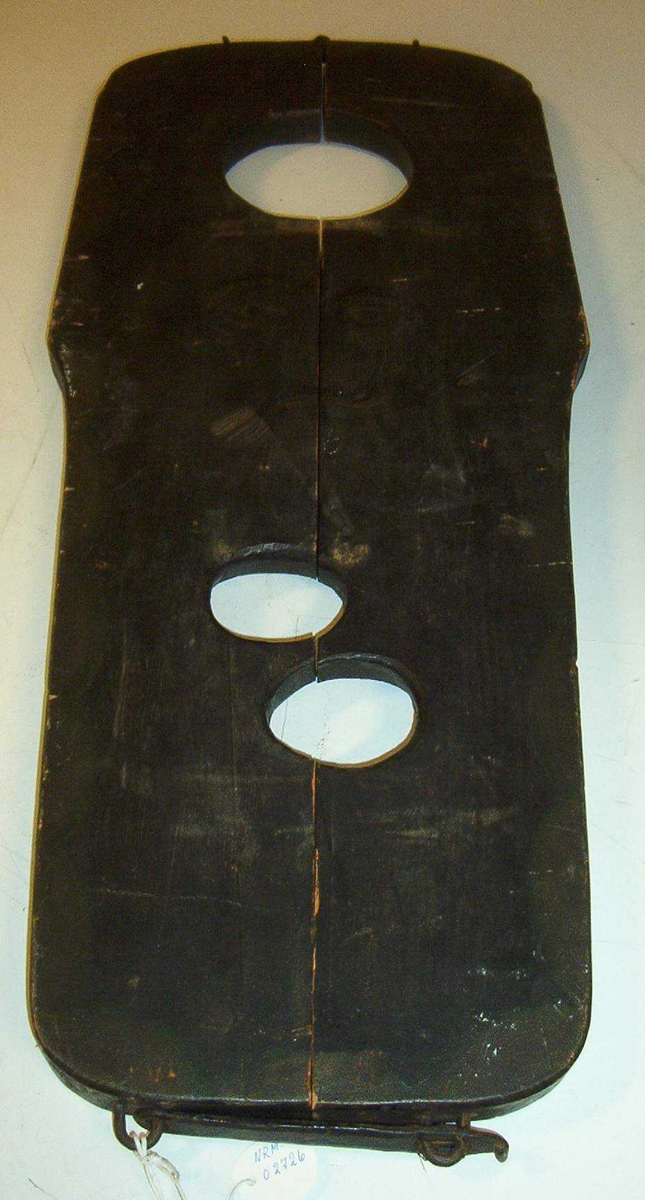 Kraftig, avlang treplate. 3 hull, 1 for hodet og 2 for hender. I bredeste enden er det et hull for halsen med diameter på 14 cm. I den smaleste enden er det to hull for håndledd, ovale, 7,5 cm lange og 6 cm brede. Instrumentet er delt i lengderetningen, er hengslet i den ene enden og kan således lukkes til om delinkvintens hals og håndledd. I den andre enden kan de to halvdelene festes til hverandre med krampe og beslag for hengelås. Instrumentet er brunmalt, på oversidener et ansikt malt , rundt kanten en buet bord.