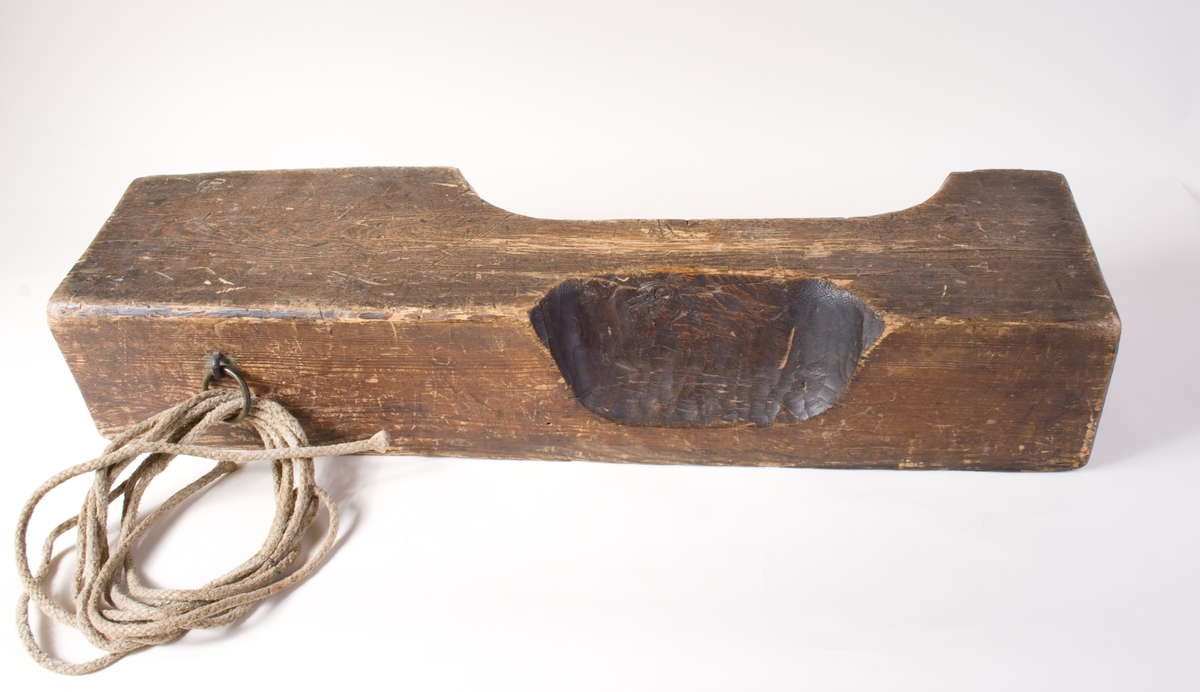 Skåret rektangulær treblokk med et smalt søkk til haken og et bredere søkk for halsen. Huggemerker og slitasje mellom de to søkkene.