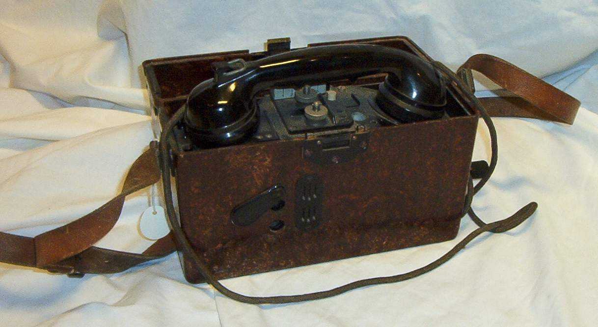 Felttelefon. Feldfernsprecher 33, FF33, tyskprodusert. Serienummer 74058.  Produksjonsår 1941. Telefonen er innebygd i bakelittkasse med bæresele. Hvit kodelapp montert på lokket. Det tyske alfabet står skrevet på lokket.