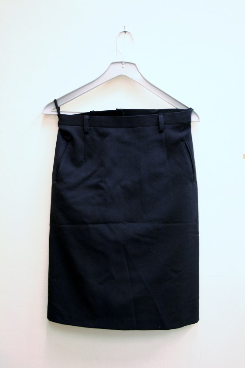 Foret, sort jakke med gullforgylte eikeløvsnåler på kraven. 4 gullforgylte knapper med riksvåpen i front og to ved splitten bak. Epåletter i flettet gull med fire stjerner og eikeløv (politidirektør). Fire lommer med klaff og knapp. Politimerke med riksvåpen på overarmene. Navneskilt i sort plast med gul skrift og riksvåpen. To ekstra navneskilt medfølger.

Knelangt, sort skjørt med glidlås bak.

Et kryssbandolær med gullforgylt rektangulær spenne dekorert med riksvåpen.

Et bredt lærbelte med gullforgylt rektangulær spenne dekorert med riksvåpen.

Et smalt lærbelte med gullforgylt rektangulær spenne dekorert med riksvåpen.

Politilue med hvit pull og luemerke i gull og rødt og eikeløvsbroderier i sort og gull. To forgylte knapper holder luesnoren på plass. (Lue for vinterhalvåret (med sort pull) registrert på NRM.03690)

Slips, skjorte og hvite hansker medfølger ikke.