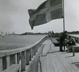 Förtöjningstrossen löper överbord. Ena änden lägges om pollaren på styrbords låring. Andra änden är belagd ytterst på hocken.