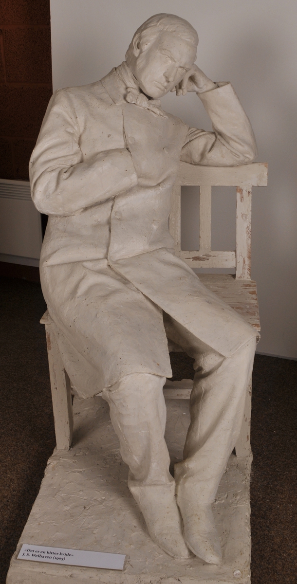 Heilfigur av diktaren J. S. Welhaven, sitjande på ein benk. Motto frå verset "det er en bitter kvide".