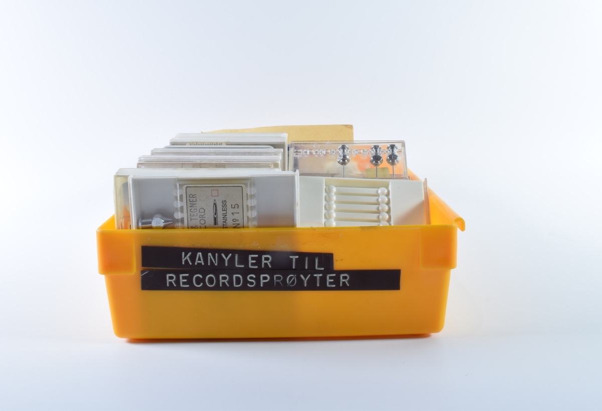 Oransje, rektangulær, plasteske uten lokk som inneholder diverse kanyler og sprøyter. 

Det er 22 kvadratiske, flate esker med kanyler i stål. 20 av eskene er av plast, hvorav 12 er i klar plast og 8 er i hvit plast med skyvelokk i klar plast. En eske er av metall og en er av papp. Antallet kanyler i eskene varierer og de er av forskjellig størrelse. Det er også tre mindre esker i plast med hvit lokk som inneholder 6 kanyler hver. En lang kanyle ligger løs.

Det er fire esker i hvit papp som inneholder hver sin sprøytesylinder uten stempel. Sprøytesylinderene er av plast. Tre er av ensartet størrelse (10cm lang eske), mens den fjerde er litt mindre (8 cm lang eske). En sprøytesylinder av glass med metallbeslag i begge endene ligger løs.

Den oransje esken inneholder også en brun papirkonvolutt med 11 bunter tynne metalltråder. På konvolutten står det "Rensenåler".