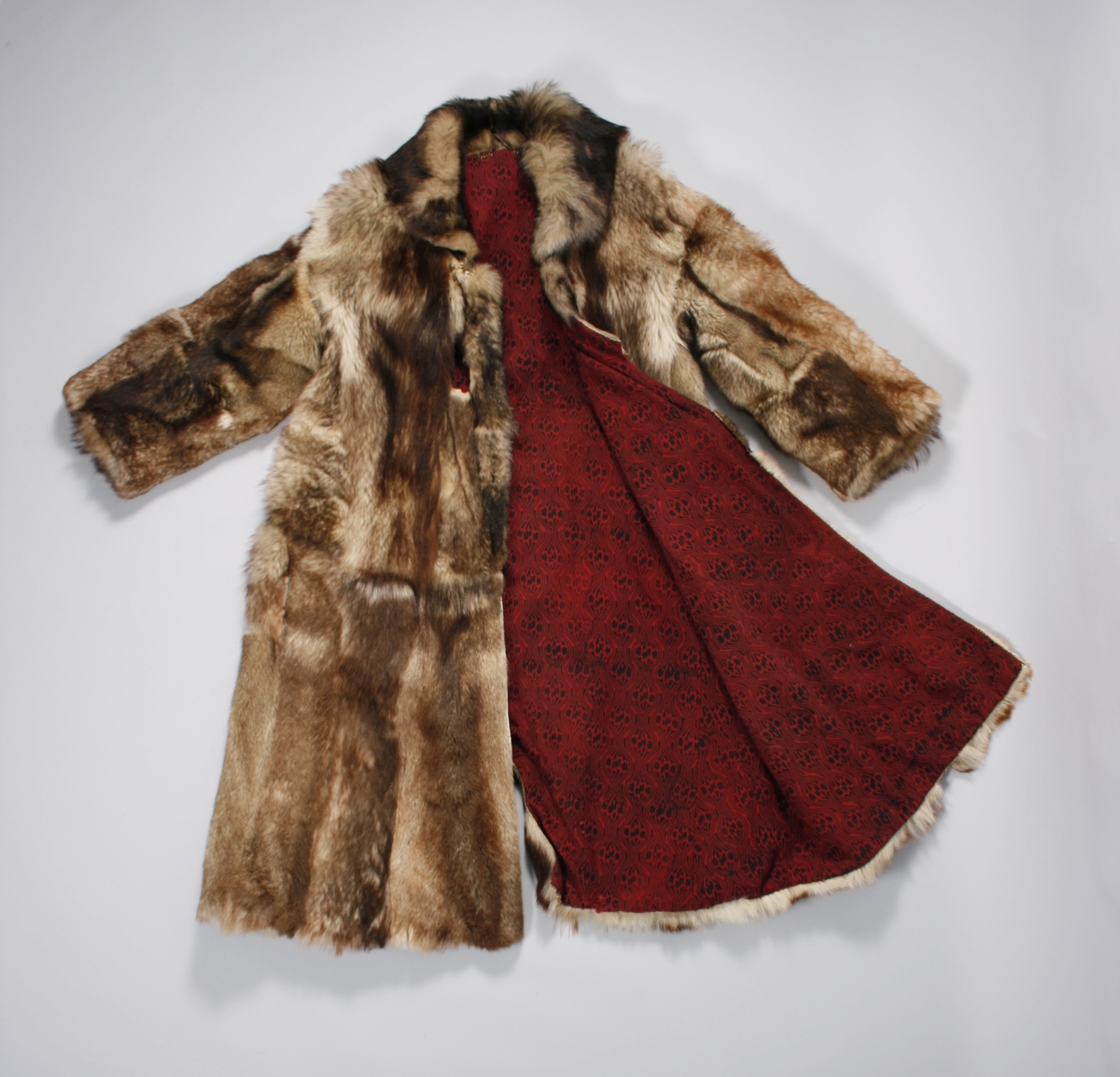 Ulveskinnspels, Lang og noe utskrådd. 
Sydd sammen av mange smale pelsstykker, to i høyden. En liten splitt midt bak. Ermer sydd sammen av mindre pelsstykker. Ermene har en liten oppbrettet fald av pelsen i nedkant, på resten av plagget er pels og fór sydd sammen kant i kant, ute belegg eller oppbrettet fald. Sjalskrage med underkrage av sort kunstpels. Underkragen har søm midt bak. 
Fóret med rødt klede med sort trykk, også i ermene.
Hele plagget er håndsydd med grov tråd, selve pelsen med ubleket lintråd. Fóret er sydd sammen, og sydd til pelsen, med ubleket eller sort bomullstråd. Fóret har sidesømmer, men ingen søm i ryggen. Ryggstykket er kvadratisk med trådrette sider. Forstykkene er trådrette midt foran og skrådd i siden. I sidene er det satt inn en liten kile nederst. 
I nedkant av kragen i venstre side er det en stor sølvhekte, gravert med blomstermotiv. Ingen tegn til annen lukning.  
Stor lærhempe i nakken.