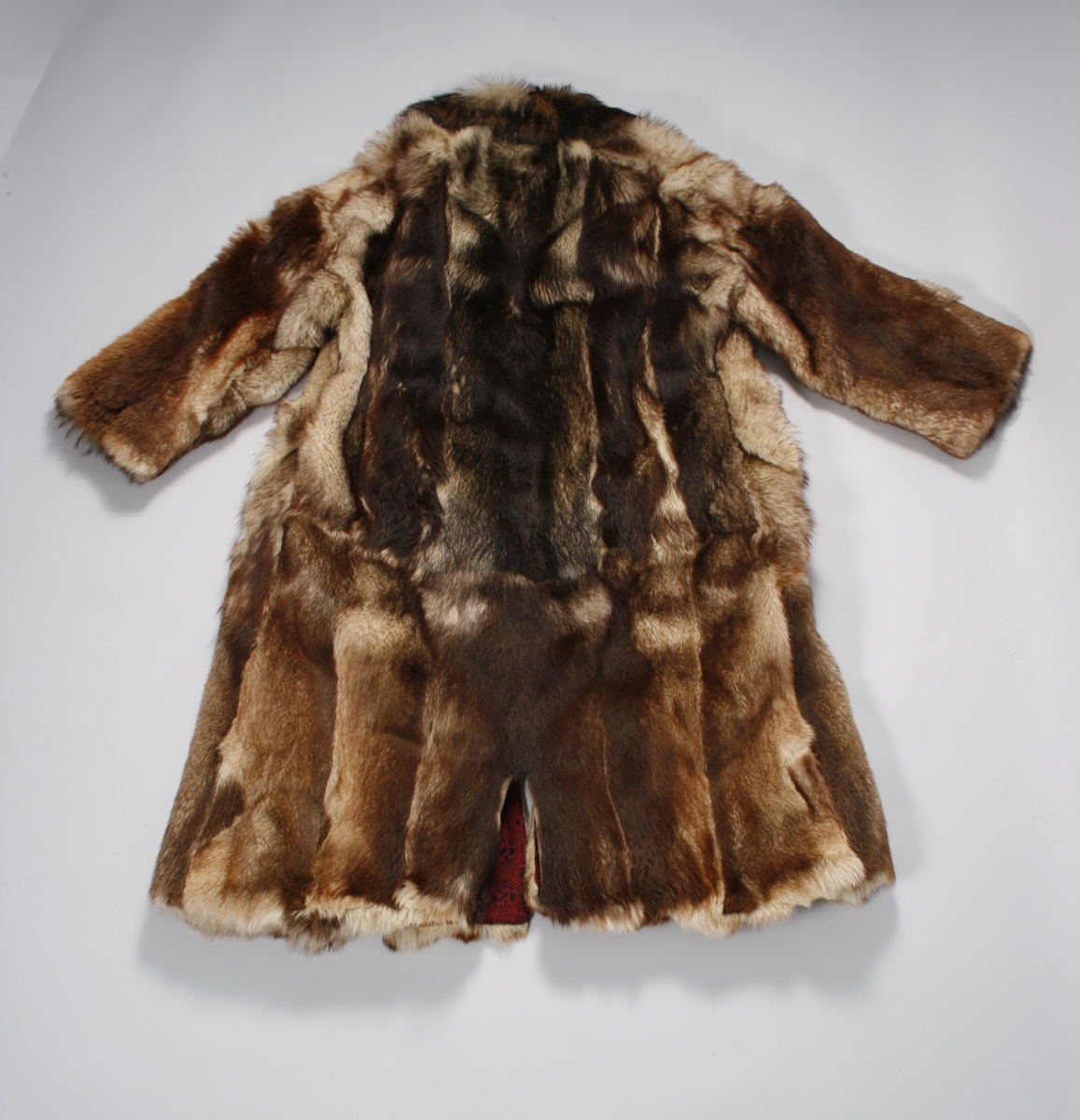 Ulveskinnspels, Lang og noe utskrådd. 
Sydd sammen av mange smale pelsstykker, to i høyden. En liten splitt midt bak. Ermer sydd sammen av mindre pelsstykker. Ermene har en liten oppbrettet fald av pelsen i nedkant, på resten av plagget er pels og fór sydd sammen kant i kant, ute belegg eller oppbrettet fald. Sjalskrage med underkrage av sort kunstpels. Underkragen har søm midt bak. 
Fóret med rødt klede med sort trykk, også i ermene.
Hele plagget er håndsydd med grov tråd, selve pelsen med ubleket lintråd. Fóret er sydd sammen, og sydd til pelsen, med ubleket eller sort bomullstråd. Fóret har sidesømmer, men ingen søm i ryggen. Ryggstykket er kvadratisk med trådrette sider. Forstykkene er trådrette midt foran og skrådd i siden. I sidene er det satt inn en liten kile nederst. 
I nedkant av kragen i venstre side er det en stor sølvhekte, gravert med blomstermotiv. Ingen tegn til annen lukning.  
Stor lærhempe i nakken.