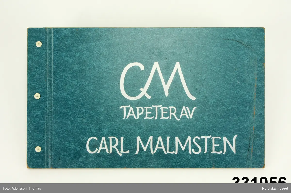 Tapetprovbok med pärm av blå papp. På pärmens utsida vit text: "CM TAPETER AV CARL MALMSTEN". På försättsbladet information om vilka mönster som ingår i kollektionen: Skogaholm, Haga, Campagna, Korsblomma, Fågel Blå och Tussilago, åtminstone de tre sista formgivna 1917. På samma blad samt på den främre pärmens insida klisteretiketter med texten: "INTER-ZETHA AB. Berzelii Park 11, 114 47 STOCKHOLM" samt telefonnummer.

Provboken innehåller prover på papperstapeter med stiliserade och naturalistiska blomstermönster, geometriska figurer och randmönster med inskrivna klassicistiska motiv. De flesta mönster i smutsiga pastellfärger. Alla tapeter tryckta på slätt papper och plastbehandlade. Uppgift om tillverkare saknas.

Anm.
Ett tapetprov utskuret, ligger löst på sin plats i boken. Tapetprovboken har tidigare använts av C. A. Kåbergs tapetaffär J.V. Modin A.B., Regeringsgatan 5 i Stockholm, visar stämplar på försättsblad och pärmar i boken.
/Maria Maxén 2013-10-10