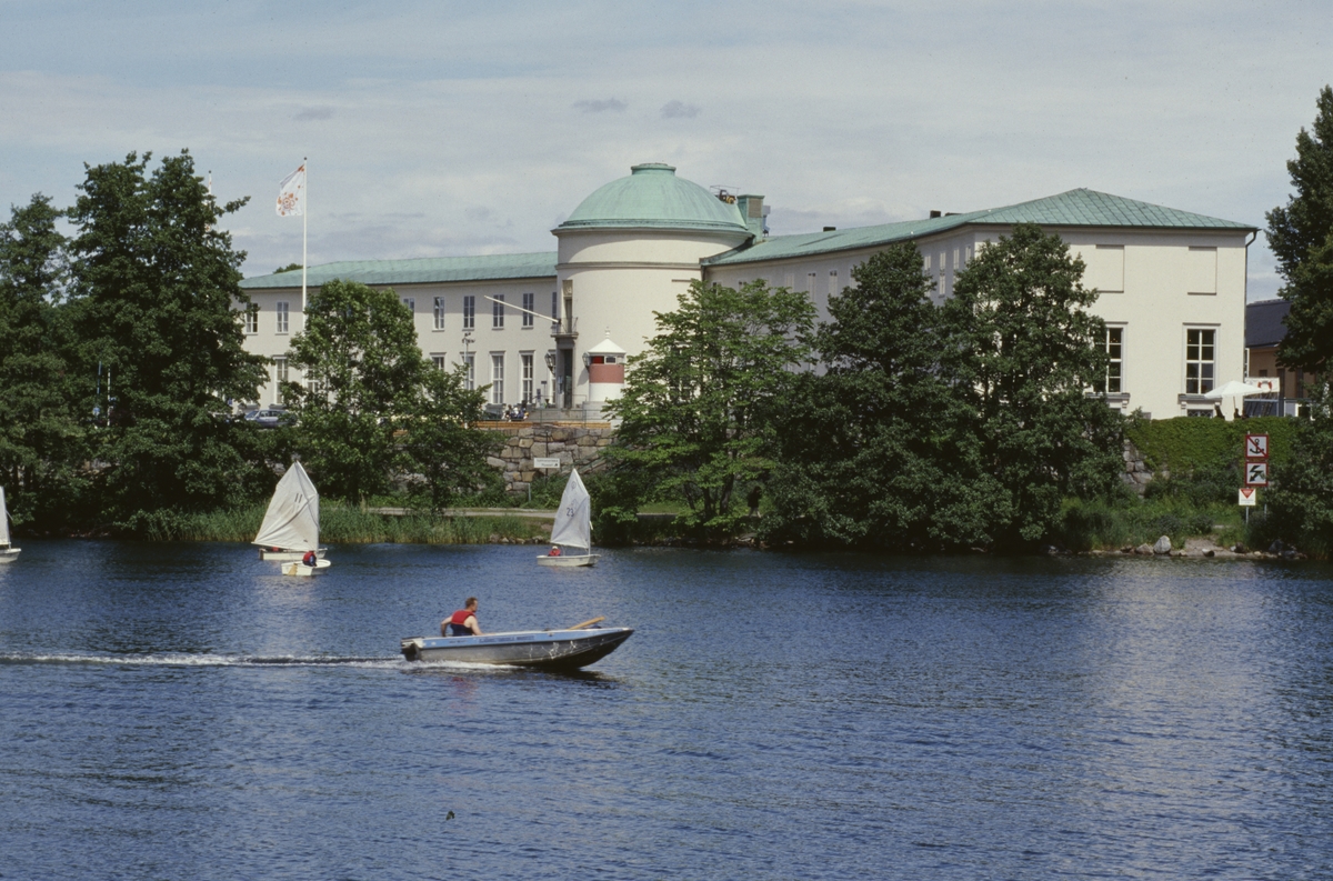 Sjöhistoriska museet sett från Djurgårdsbrunnsviken. Motorbåt och optimistjollar från museets seglarskola på vattnet i förgrunden.