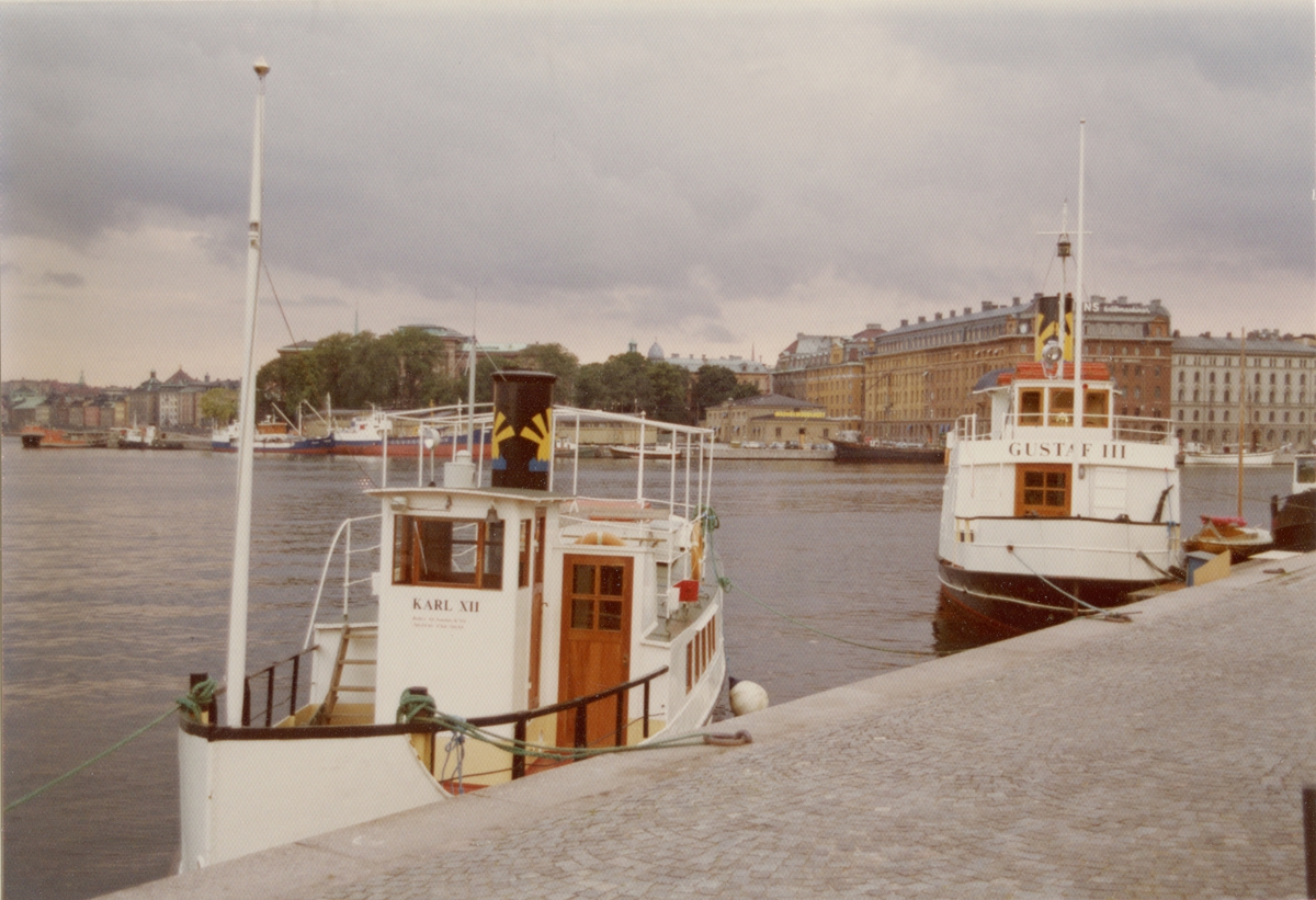 Foto i färg visande passagerarmotorfartygen Karl XII och Gustav III av Stockholm vid Strandvägskajen, Stockholm 1974. samt m/s Karl XII
