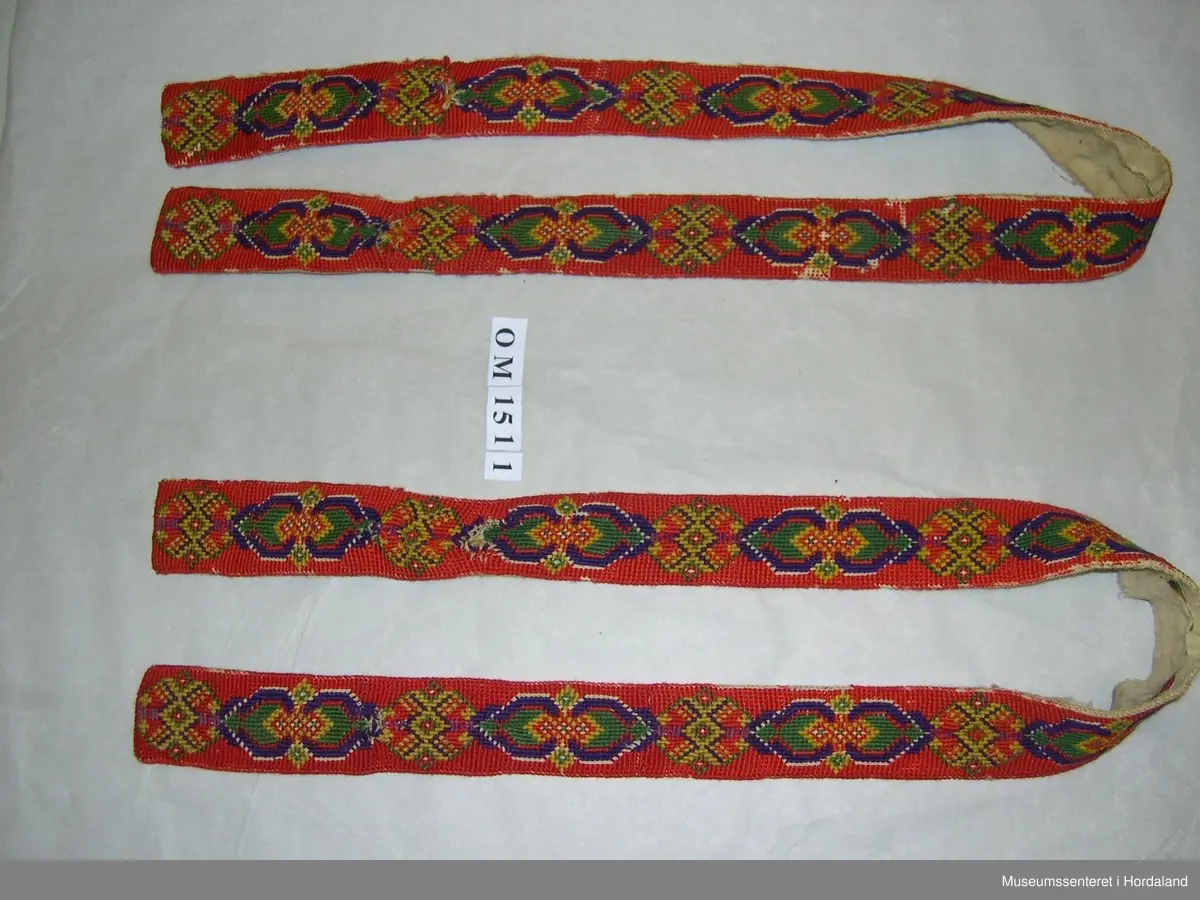 Eit par mannsseler brodert med halve krossting. Hovudfarge er raud, med mønsterdekor i lilla, grønt og gult. Her er òg felt som ikkje er sydd slik at den ubleika strameifargen under kjem fram. Selane har hemper på baksida til festing på buksa. Litt slitt.