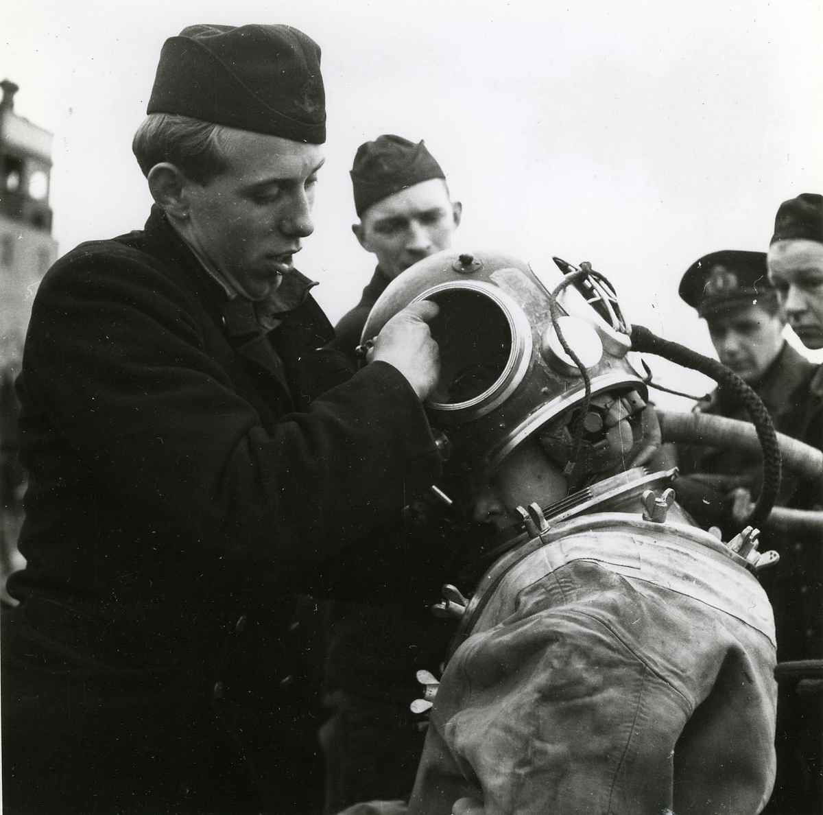 Utrustning av dykare på ubåten Sjöormen vid Skeppsholmen 1949.
Hjälmen sättes på.