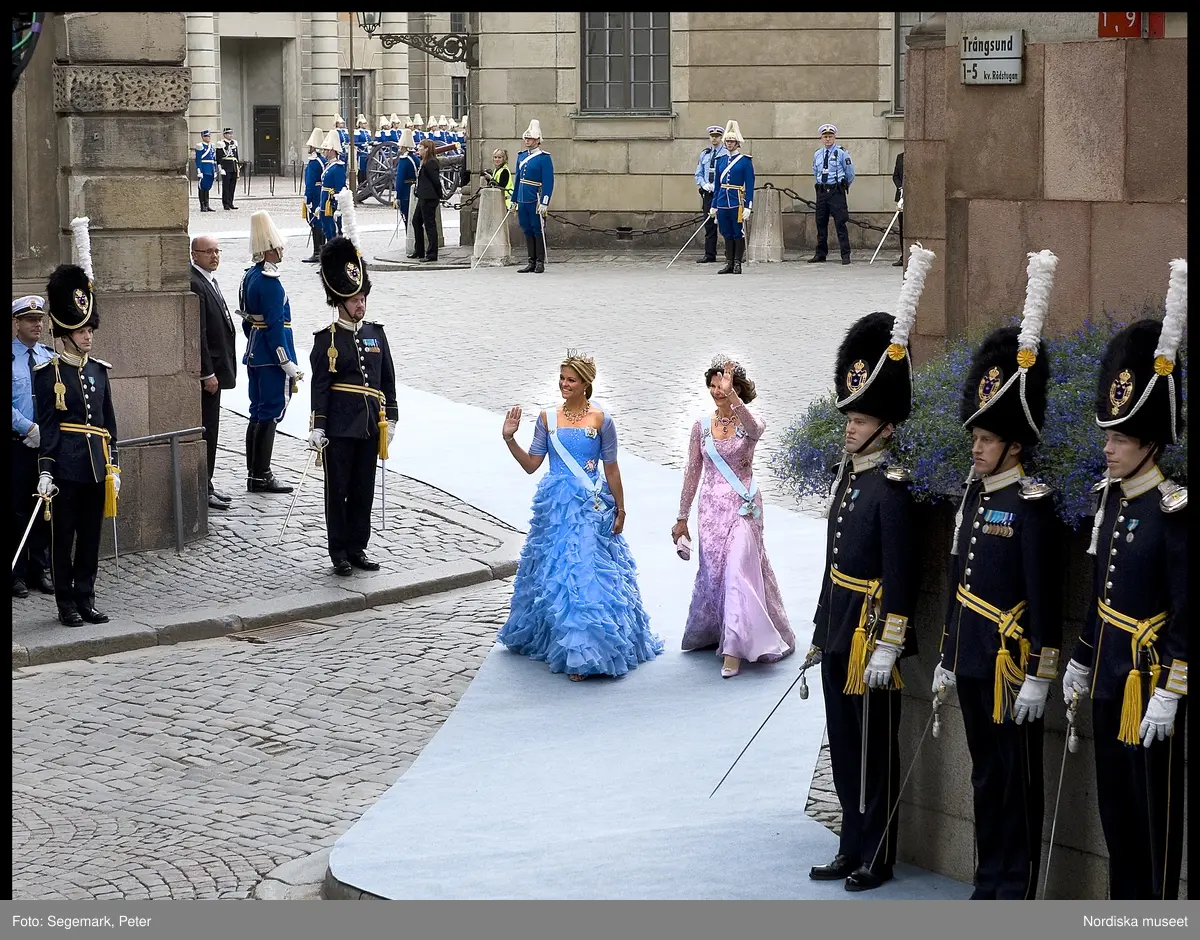 Kronprinsessbröllopet. Dokumentation av bröllopet mellan Kronprinsessan Victoria och herr Daniel Westling 19 juni 2010. Gästerna anländer till Storkyrkan. Drottning Silvia i rosa tyllklänning med pärl-och stenbroderier och silvrig calaisspets, det brasilianska diademet, halsband, örhängen och brosch av diamanter och rosa ädeltopaser, ordenstecken. Prinsessan Madeleine i förgätmigej-blå chiffongklänning med kristallbroderat liv, prinsessan Sibyllas diadem av fem blomsterkransar i briljanter och dallrande briljantkläppar, halsband-intågssmycket uppbyggt av ceylonsafirer, barockpärlor och briljanter, ordenstecken.