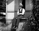 Man sittande utanför hus i sommarhatt.