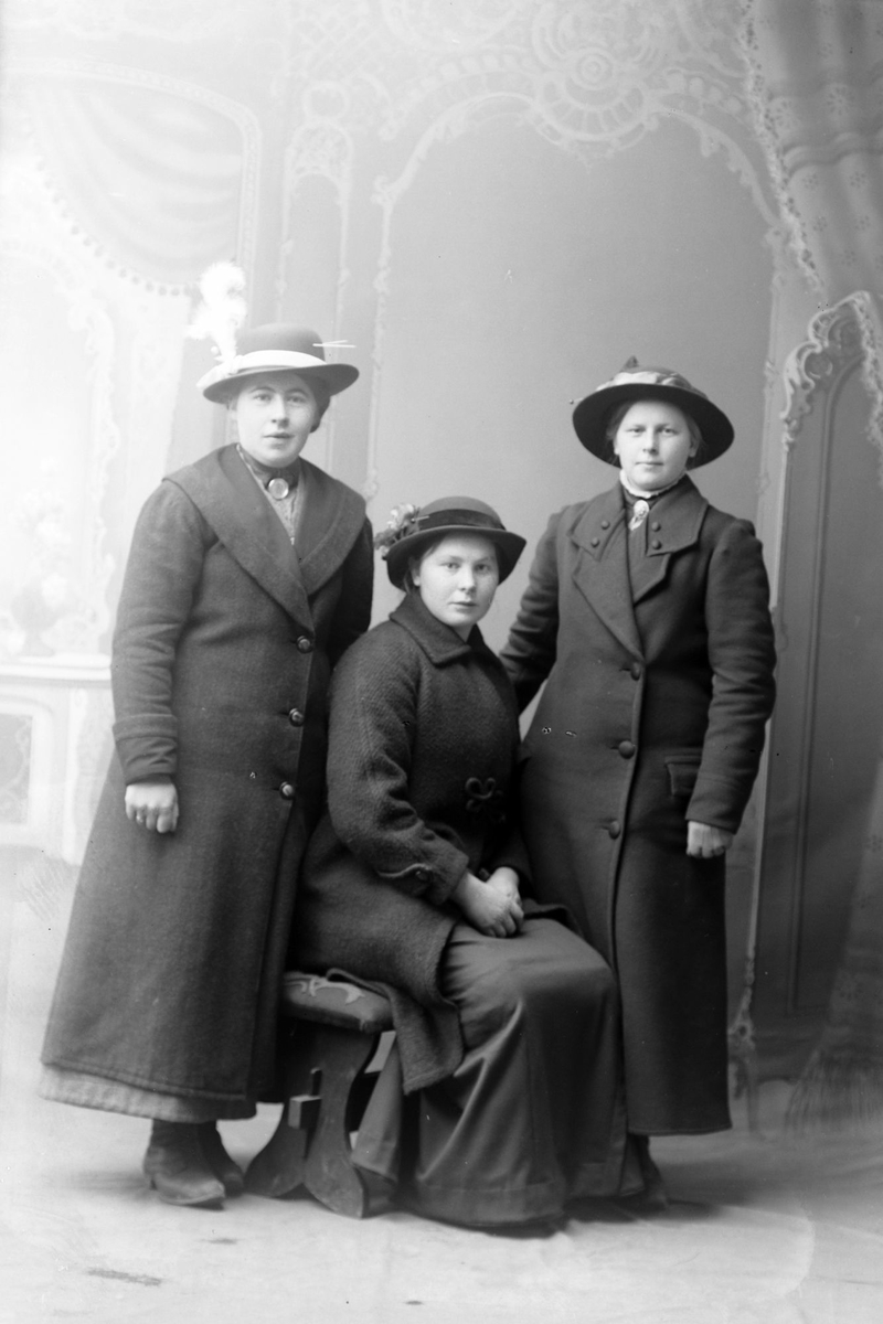 Studioportrett av tre kvinner ikledd lange kåper.