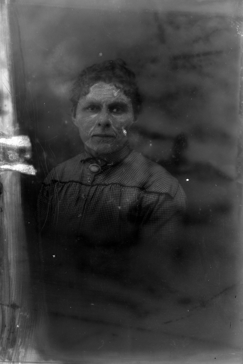 Studioportrett av en kvinne i halvfigur. Bildet er delvis ødelagt.