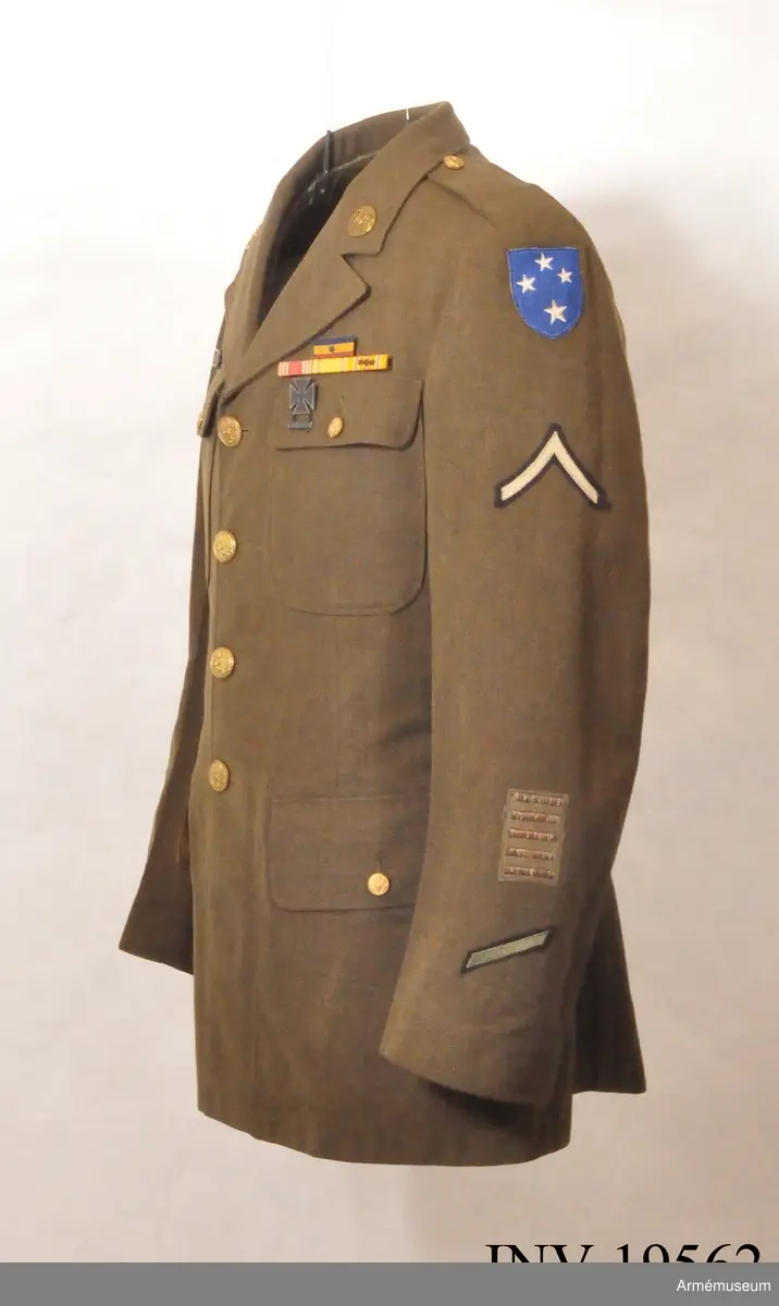 Vapenrock för amerikanska infanteriet. En class A uniform. Vapenrocken är från andra världskriget. Den är  enkelknäppt med 4 metallknappar och har  4 st utanpåfickor med lock. Framsidans insida är fodrad med bomullsväv. Axelklaffarna har inga emblem. På kragspegeln finns en  knapp märkt US. Vänster ärms övre del har ett märke med 4 st stjärnor och ett emblem (ett upp-och nedvänt V) som anger korprals grad. Längre ner finns 5 broderade band som anger " overseas service" och underst ett snedställt streck för 3 års tjänstgöring. Höger ärm har överst ett emblem för koprals grad, och längre ner ett märke: på blå botten med stjärnor och texten Guadalcanal.  Släpspännen: Unit citation with star 31 dec 43 Issued laped button - No time lost under AWL American Defence Service Medal, Asiatic Pacific Theatre Campaign Ribbon with two Service stars. Vapenrocken har tillhört Per Rabe under hans tjänstgöring i amerikanska armén under andra världskriget.