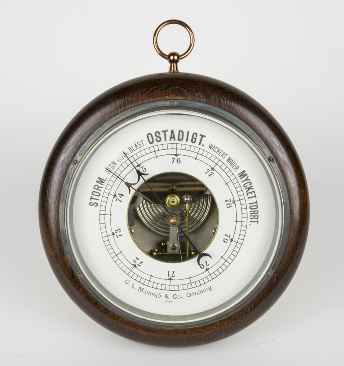 Barometer som liknar en klocka. Barometern har en träram och en vit urtavla. På tavlan finns en graf som går från Storm till Ostadigt och vidare till Mycket torrt.