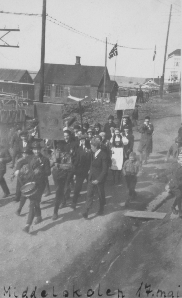 'Russetog' 17. mai 1926. Med elever fra Middelskolen i Vadsø. Den fremste gutten slår på en tromme. Knut Evanger går like bak den første 'fanen'. Martha Dahl er kledt i bunad. Bakerst går Rønnaug Jakobsen. Bildet er tatt fra Havnegata. Evangers hus ses helt til høyre. Nedenfor dette ligger huset til Nordahl. I huset midt på bildet var det trykkeri. Flaggene er heist på flaggstenger