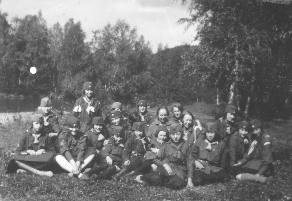 Jentespeider fra blant annet Vadsø på Kretsleir i Alta, 1928. Her er de på tur i skogen. Jenta i bakerste rekke, med hårfletter, er Tora Dahl. Omtrent midt i bildet sitter, Gjertrud Evanger, Sara Vikki, og Herdis Abrahamsen. Det er trær i bakgrunnen