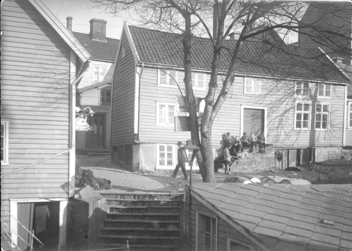 Møllerveien, nedgang til Eidebryggen, 1930-årene. Skipper Madsens hus, "Madsahuset". Foran i bildet er en trapp. Oppe til venstre for trappen ligger garnkveil/not, på høyre side tønner, stor gammel gatelykt på høyre side, nyere elektrisk til venstre over butikkskiltet: "Oxanoljen kleber ikke". I bakgrunnen ses tett bybebyggelse. Bak til høyre er indremisjonshotellet.