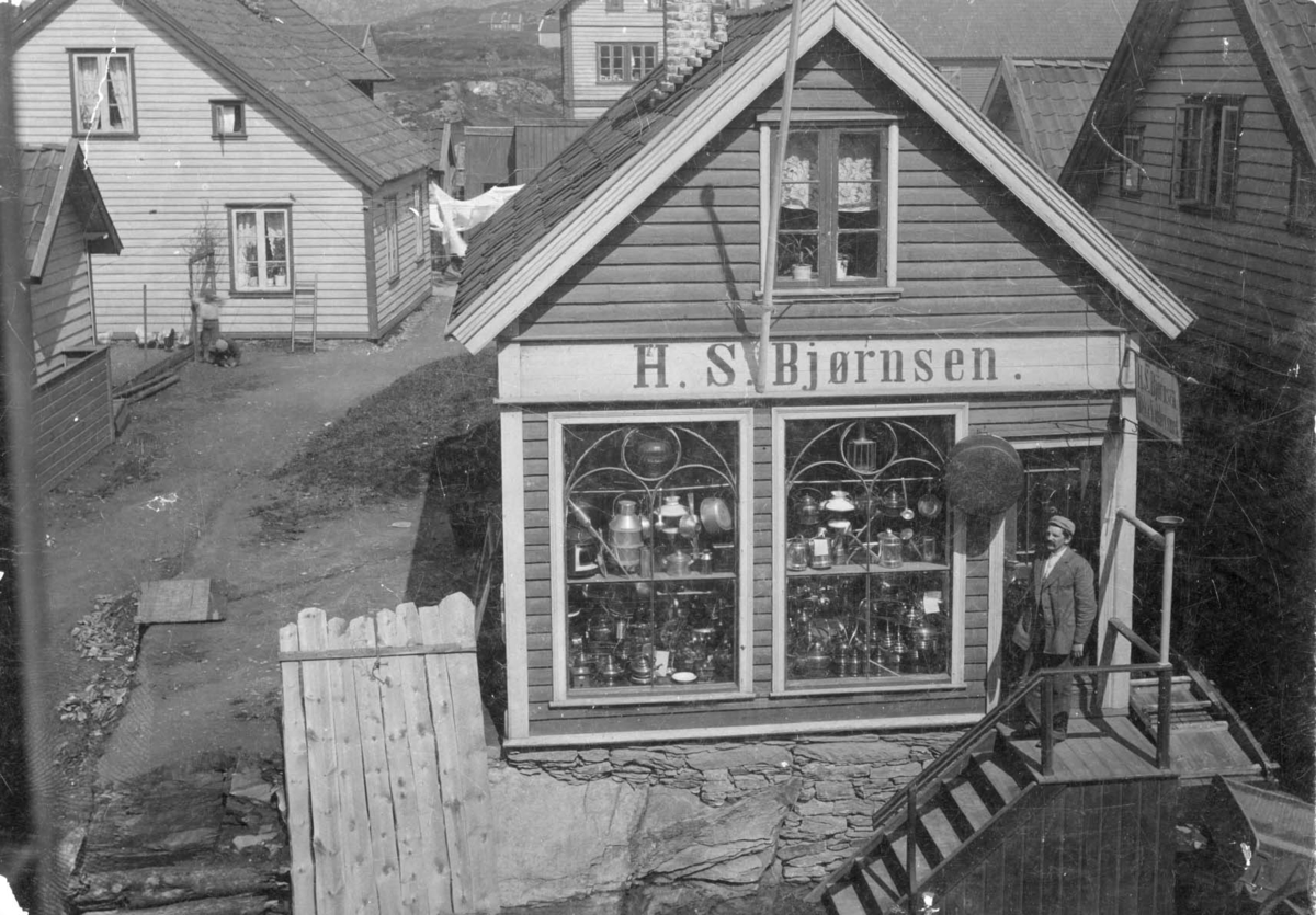 Kobberslagforretningen H. S. Bjørnsen Ved trappen og i smuget to hestekjerrer. Til v. ligger en lem opp mot muren og ved denne går et tråkk videre gjennom et smug. Bak og rundtom ses flere hus, barn som leker og klesvask som tørker i vinden. Se også baksiden av bildet.