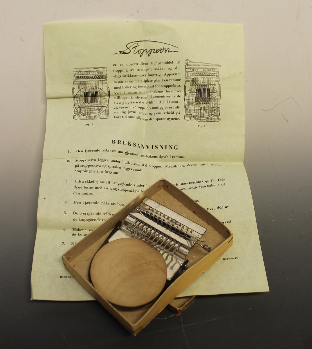Rektangulær eske med "Stopper'n" og bruksanvisning oppi. brukt til å stoppe hull i strømper, sokker og alle strikket plagg.