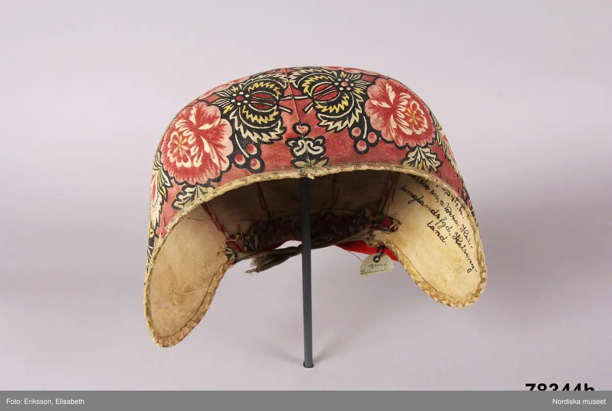 Huvudliggaren:
"Kvinnodräkt fr. Delsbo sn, Norra Helsinglands fgd, Helsingland.
a. "Ryntjeskjortel" af svart kläde med röd kant och bandväfd "kval" (linning). Kjolen "lurad"(goffrerad), skall förvaras lurad att ej vecken gå ut. 3 par fruntimmershänder hjälpas åt att "lura" den efter hvarje begagnande.
b. livstycke, rött med gröna ränder.
c. "Ryntjessärk" (rynksärk) af hvitt bomullstyg med "krus" (handbroderi) kring hals och händer.Begagnas sommartiden
d. "Bumsförkläde" af ylle, blårandigt med bandväf,"kval" i rödt och grönt.
e. "Förklesband" rödt och grönt ylle med "doppar" (tofsar) i ändarna. Lindas 1 à 2 hvarf kring lifvet och bindes framtill med stora nedhängande "locor" och ändar. Längd 262 cm, bredd 3,4 cm.
f. Kjolsäck med mässingslås och hake samt tennbroderi. Häktas under förklesbandet och hänger delvis under "försklet". Begagnas vanligen till förvaring af kyrkkryddor m.fl. kyrk-ellerkalassaker.
g. Halfhandskar af svart kläde med silkesbroderi. Begagnas sommartiden.
h. "Påshufva" hvardagsmössa af brokigt kattun. Begagnas med i nacken utslaget hår med några hårtestar hängande fritt framför öronen.
Till dräkten användes röda strumpor samt låga skor med höga klackar. Äfven kan användas silfersmycken kring halsen eller å  bröstet. En á två brokiga silkesdukar brukades omkring halsen nedstoppade under lifstycket, så att kruset kring halsen  på "ryntjessärken" sammanfästadt med ett löfspänne samt en smalare kant af hvarje sidenduk, blevo synliga. Vid handlederna sammanfästes ryntjessärken med röda sidenband eller länkknappar.

a. KJOL 
längd: 87 cm
midjeband bredd: 7 cm
av svart halvylle med svart linvarp och inslag av svart 1-tr. ullgarn, de 2 yttersta stadtrådarna är av oblekt lingarn. 4 goffrerade våder samt en slät framvåd som skarvats under förklädet med oblekt bomullslärft. 5 cm bred list av rött kläde i nederkanten runtom. Brett midjeband mönstervävt i rött och grönt ullgarn och vitt bomullsgarn. Knäppt vid framvådens vänstra sida med 2 hakar och hyskor av mässing.
b. LIVSTYCKE
längd: 39 cm
av halvylle i varptäckande kypert, varp av vitt lingarn, inslag av svart och grönt ullgarn med flaminslag av vitt, 2 fram-och sidstycken, 2 bakstycken avsmalnande till skörtveck med tre par tränsade förstärkningar av svart garn. I midjehöjd ett avsytt veck runtom, knäppt kant i kant med 8 par grova hakar och hyskor av mässing. Foder av ofärgad bomullslärft.
BE

c. ÖVERDEL
Längd: 39 cm. Längd: 58 cm - ärmlängd. Vidd: 56 cm - ärmvidd. Vidd: 114 cm. Höjd: 1,7 cm - kraghöjd. Material: Textil, bomull. Textil, linne - ärmlinning, krage. Bomullsgarn - broderi. Telnik: Tuskaft. Trådbundet broderi. Broderi, rätlinjig plattsöm. Handsömnad.
Överdel av tuskaftat vitt bomullstyg. Dubbelvikt bålstycke, isydda rektangulära halsspjäll. Täta breda stripade  rynkor mot halskrage i bomull, 1,7 cm hög. Kragen har broderier i rätlinjig plattsöm, vitt bomullsgarn över hela ytan, nuggor i kanten, langetterade bågar  i framkant. 16 cm långt sprund fram, tränsad förstärkning nedtill, 3 cm.  Vidsydd ärm med  infällda ärmspjäll, lagda veck över axeln fram och bak. Täta breda stripade rynkor mot 2,5 cm bred ärmlinning. Ärmlinningen har yttäckande vita broderier i rätlinjig plattsöm, rombiska former. Vita knytband i bomull i ärmlinningar och krage. Överdelen är handsydd.
/Inga-Lill Eliasson 2007-11-26


d. FÖRKLÄDE
längd=vådbredd: 82 cm
bredd: 97,5 cm
av halvylle, varp av svart lingarn, inslag i varptäckande kypert av svart 1-tr. ullgarn med smala ränder istarkt blått och en knappt synlig svart tråd med vita flamgarnsfläckar av bomull. Upptill stripade rynkor där de blå bårderna utnyttjats dekorativt i rynkningen. Mönstervävt midjeband i grönt på rött ullgarn , bandet knäpps med 2 hakar och hyskor i vänster sida.
I nederkantens båda hörn infodringar på insidan av svart bomullslärft, för att tyget inte skall rulla sig.



Berit Eldvik 2004