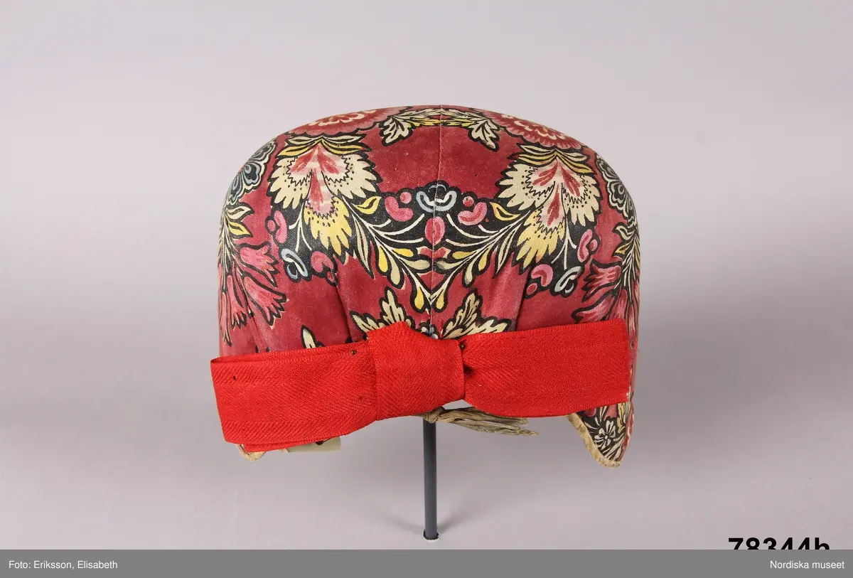 Huvudliggaren:
"Kvinnodräkt fr. Delsbo sn, Norra Helsinglands fgd, Helsingland.
a. "Ryntjeskjortel" af svart kläde med röd kant och bandväfd "kval" (linning). Kjolen "lurad"(goffrerad), skall förvaras lurad att ej vecken gå ut. 3 par fruntimmershänder hjälpas åt att "lura" den efter hvarje begagnande.
b. livstycke, rött med gröna ränder.
c. "Ryntjessärk" (rynksärk) af hvitt bomullstyg med "krus" (handbroderi) kring hals och händer.Begagnas sommartiden
d. "Bumsförkläde" af ylle, blårandigt med bandväf,"kval" i rödt och grönt.
e. "Förklesband" rödt och grönt ylle med "doppar" (tofsar) i ändarna. Lindas 1 à 2 hvarf kring lifvet och bindes framtill med stora nedhängande "locor" och ändar. Längd 262 cm, bredd 3,4 cm.
f. Kjolsäck med mässingslås och hake samt tennbroderi. Häktas under förklesbandet och hänger delvis under "försklet". Begagnas vanligen till förvaring af kyrkkryddor m.fl. kyrk-ellerkalassaker.
g. Halfhandskar af svart kläde med silkesbroderi. Begagnas sommartiden.
h. "Påshufva" hvardagsmössa af brokigt kattun. Begagnas med i nacken utslaget hår med några hårtestar hängande fritt framför öronen.
Till dräkten användes röda strumpor samt låga skor med höga klackar. Äfven kan användas silfersmycken kring halsen eller å  bröstet. En á två brokiga silkesdukar brukades omkring halsen nedstoppade under lifstycket, så att kruset kring halsen  på "ryntjessärken" sammanfästadt med ett löfspänne samt en smalare kant af hvarje sidenduk, blevo synliga. Vid handlederna sammanfästes ryntjessärken med röda sidenband eller länkknappar.

a. KJOL 
längd: 87 cm
midjeband bredd: 7 cm
av svart halvylle med svart linvarp och inslag av svart 1-tr. ullgarn, de 2 yttersta stadtrådarna är av oblekt lingarn. 4 goffrerade våder samt en slät framvåd som skarvats under förklädet med oblekt bomullslärft. 5 cm bred list av rött kläde i nederkanten runtom. Brett midjeband mönstervävt i rött och grönt ullgarn och vitt bomullsgarn. Knäppt vid framvådens vänstra sida med 2 hakar och hyskor av mässing.
b. LIVSTYCKE
längd: 39 cm
av halvylle i varptäckande kypert, varp av vitt lingarn, inslag av svart och grönt ullgarn med flaminslag av vitt, 2 fram-och sidstycken, 2 bakstycken avsmalnande till skörtveck med tre par tränsade förstärkningar av svart garn. I midjehöjd ett avsytt veck runtom, knäppt kant i kant med 8 par grova hakar och hyskor av mässing. Foder av ofärgad bomullslärft.
BE

c. ÖVERDEL
Längd: 39 cm. Längd: 58 cm - ärmlängd. Vidd: 56 cm - ärmvidd. Vidd: 114 cm. Höjd: 1,7 cm - kraghöjd. Material: Textil, bomull. Textil, linne - ärmlinning, krage. Bomullsgarn - broderi. Telnik: Tuskaft. Trådbundet broderi. Broderi, rätlinjig plattsöm. Handsömnad.
Överdel av tuskaftat vitt bomullstyg. Dubbelvikt bålstycke, isydda rektangulära halsspjäll. Täta breda stripade  rynkor mot halskrage i bomull, 1,7 cm hög. Kragen har broderier i rätlinjig plattsöm, vitt bomullsgarn över hela ytan, nuggor i kanten, langetterade bågar  i framkant. 16 cm långt sprund fram, tränsad förstärkning nedtill, 3 cm.  Vidsydd ärm med  infällda ärmspjäll, lagda veck över axeln fram och bak. Täta breda stripade rynkor mot 2,5 cm bred ärmlinning. Ärmlinningen har yttäckande vita broderier i rätlinjig plattsöm, rombiska former. Vita knytband i bomull i ärmlinningar och krage. Överdelen är handsydd.
/Inga-Lill Eliasson 2007-11-26


d. FÖRKLÄDE
längd=vådbredd: 82 cm
bredd: 97,5 cm
av halvylle, varp av svart lingarn, inslag i varptäckande kypert av svart 1-tr. ullgarn med smala ränder istarkt blått och en knappt synlig svart tråd med vita flamgarnsfläckar av bomull. Upptill stripade rynkor där de blå bårderna utnyttjats dekorativt i rynkningen. Mönstervävt midjeband i grönt på rött ullgarn , bandet knäpps med 2 hakar och hyskor i vänster sida.
I nederkantens båda hörn infodringar på insidan av svart bomullslärft, för att tyget inte skall rulla sig.



Berit Eldvik 2004