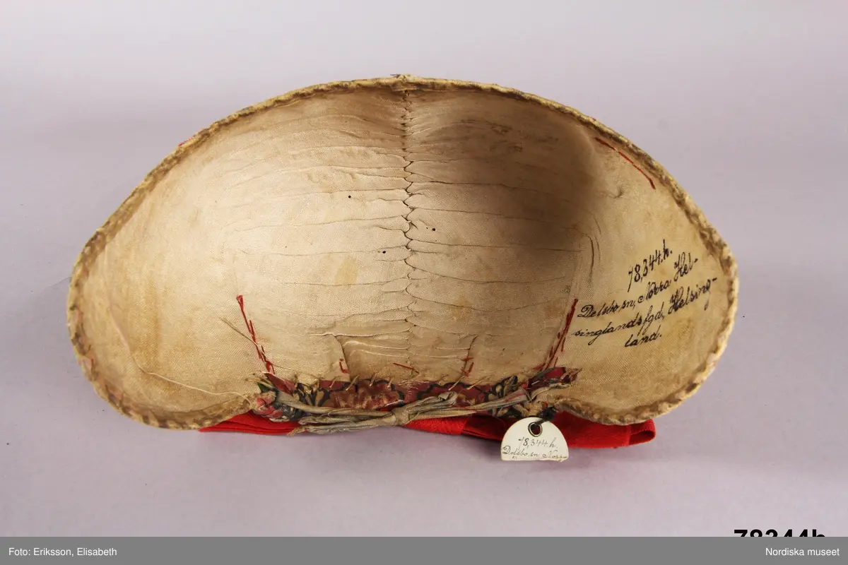 Huvudliggaren:
"Kvinnodräkt fr. Delsbo sn, Norra Helsinglands fgd, Helsingland.
a. "Ryntjeskjortel" af svart kläde med röd kant och bandväfd "kval" (linning). Kjolen "lurad"(goffrerad), skall förvaras lurad att ej vecken gå ut. 3 par fruntimmershänder hjälpas åt att "lura" den efter hvarje begagnande.
b. livstycke, rött med gröna ränder.
c. "Ryntjessärk" (rynksärk) af hvitt bomullstyg med "krus" (handbroderi) kring hals och händer.Begagnas sommartiden
d. "Bumsförkläde" af ylle, blårandigt med bandväf,"kval" i rödt och grönt.
e. "Förklesband" rödt och grönt ylle med "doppar" (tofsar) i ändarna. Lindas 1 à 2 hvarf kring lifvet och bindes framtill med stora nedhängande "locor" och ändar. Längd 262 cm, bredd 3,4 cm.
f. Kjolsäck med mässingslås och hake samt tennbroderi. Häktas under förklesbandet och hänger delvis under "försklet". Begagnas vanligen till förvaring af kyrkkryddor m.fl. kyrk-ellerkalassaker.
g. Halfhandskar af svart kläde med silkesbroderi. Begagnas sommartiden.
h. "Påshufva" hvardagsmössa af brokigt kattun. Begagnas med i nacken utslaget hår med några hårtestar hängande fritt framför öronen.
Till dräkten användes röda strumpor samt låga skor med höga klackar. Äfven kan användas silfersmycken kring halsen eller å  bröstet. En á två brokiga silkesdukar brukades omkring halsen nedstoppade under lifstycket, så att kruset kring halsen  på "ryntjessärken" sammanfästadt med ett löfspänne samt en smalare kant af hvarje sidenduk, blevo synliga. Vid handlederna sammanfästes ryntjessärken med röda sidenband eller länkknappar.

a. KJOL 
längd: 87 cm
midjeband bredd: 7 cm
av svart halvylle med svart linvarp och inslag av svart 1-tr. ullgarn, de 2 yttersta stadtrådarna är av oblekt lingarn. 4 goffrerade våder samt en slät framvåd som skarvats under förklädet med oblekt bomullslärft. 5 cm bred list av rött kläde i nederkanten runtom. Brett midjeband mönstervävt i rött och grönt ullgarn och vitt bomullsgarn. Knäppt vid framvådens vänstra sida med 2 hakar och hyskor av mässing.
b. LIVSTYCKE
längd: 39 cm
av halvylle i varptäckande kypert, varp av vitt lingarn, inslag av svart och grönt ullgarn med flaminslag av vitt, 2 fram-och sidstycken, 2 bakstycken avsmalnande till skörtveck med tre par tränsade förstärkningar av svart garn. I midjehöjd ett avsytt veck runtom, knäppt kant i kant med 8 par grova hakar och hyskor av mässing. Foder av ofärgad bomullslärft.
BE

c. ÖVERDEL
Längd: 39 cm. Längd: 58 cm - ärmlängd. Vidd: 56 cm - ärmvidd. Vidd: 114 cm. Höjd: 1,7 cm - kraghöjd. Material: Textil, bomull. Textil, linne - ärmlinning, krage. Bomullsgarn - broderi. Telnik: Tuskaft. Trådbundet broderi. Broderi, rätlinjig plattsöm. Handsömnad.
Överdel av tuskaftat vitt bomullstyg. Dubbelvikt bålstycke, isydda rektangulära halsspjäll. Täta breda stripade  rynkor mot halskrage i bomull, 1,7 cm hög. Kragen har broderier i rätlinjig plattsöm, vitt bomullsgarn över hela ytan, nuggor i kanten, langetterade bågar  i framkant. 16 cm långt sprund fram, tränsad förstärkning nedtill, 3 cm.  Vidsydd ärm med  infällda ärmspjäll, lagda veck över axeln fram och bak. Täta breda stripade rynkor mot 2,5 cm bred ärmlinning. Ärmlinningen har yttäckande vita broderier i rätlinjig plattsöm, rombiska former. Vita knytband i bomull i ärmlinningar och krage. Överdelen är handsydd.
/Inga-Lill Eliasson 2007-11-26


d. FÖRKLÄDE
längd=vådbredd: 82 cm
bredd: 97,5 cm
av halvylle, varp av svart lingarn, inslag i varptäckande kypert av svart 1-tr. ullgarn med smala ränder istarkt blått och en knappt synlig svart tråd med vita flamgarnsfläckar av bomull. Upptill stripade rynkor där de blå bårderna utnyttjats dekorativt i rynkningen. Mönstervävt midjeband i grönt på rött ullgarn , bandet knäpps med 2 hakar och hyskor i vänster sida.
I nederkantens båda hörn infodringar på insidan av svart bomullslärft, för att tyget inte skall rulla sig.



Berit Eldvik 2004