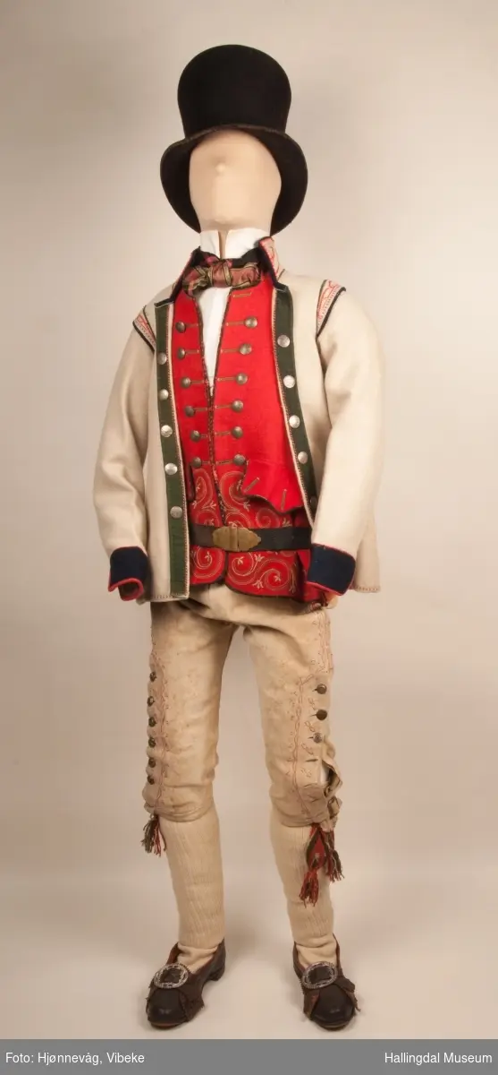 Brudgom fra Hallingdal ca. 1830. Brudgomsdrakten er satt sammen av mange plagg deriblant rød lang rød vest HFN 03616,kvit steglatrøye HFN 03615, høy hatt HFN 03086,  sokkeband HFN 01911 a-b,  knebukse HFN 2024, sko HFN 03124 a-b, skinnbelte HFN 01912, knesokker HFN 03618, kaste 03389 og silkesjal HFN 02004. Brudgommen har stått utstilt i den faste bunadutstillingen på Hallingdal Museum, Nesbyen fra 2009.