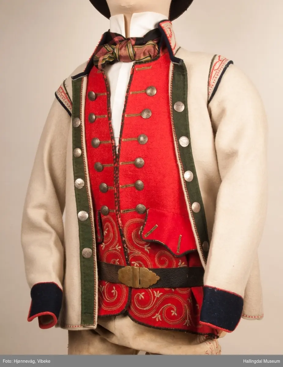 Brudgom fra Hallingdal ca. 1830. Brudgomsdrakten er satt sammen av mange plagg deriblant rød lang rød vest HFN 03616,kvit steglatrøye HFN 03615, høy hatt HFN 03086,  sokkeband HFN 01911 a-b,  knebukse HFN 2024, sko HFN 03124 a-b, skinnbelte HFN 01912, knesokker HFN 03618, kaste 03389 og silkesjal HFN 02004. Brudgommen har stått utstilt i den faste bunadutstillingen på Hallingdal Museum, Nesbyen fra 2009.