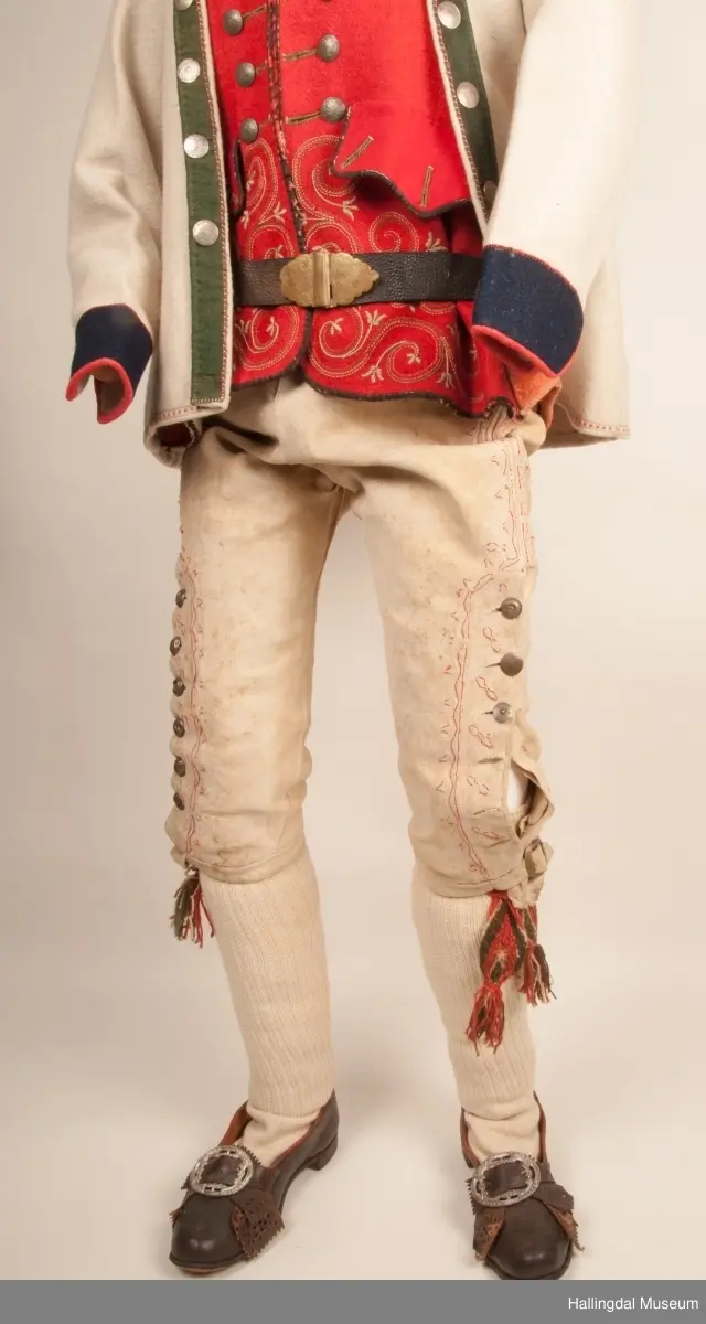 Brudgom fra Hallingdal ca. 1830. Brudgomsdrakten er satt sammen av mange plagg deriblant rød lang rød vest HFN 03616,kvit steglatrøye HFN 03615, høy hatt HFN 03086,  sokkeband HFN 01911 a-b,  knebukse HFN 2024, sko HFN 03124 a-b, skinnbelte HFN 01912, knesokker HFN 03618, kaste 03389 og silkesjal HFN 02004. Brudgommen har stått utstilt i den faste bunadutstillingen på Hallingdal Museum, Nesbyen fra 2009.