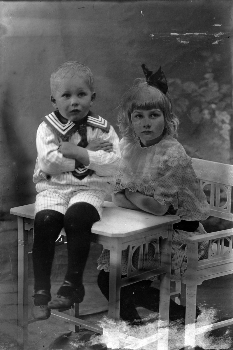 Studioportrett av to barn ved et bord og en stol.