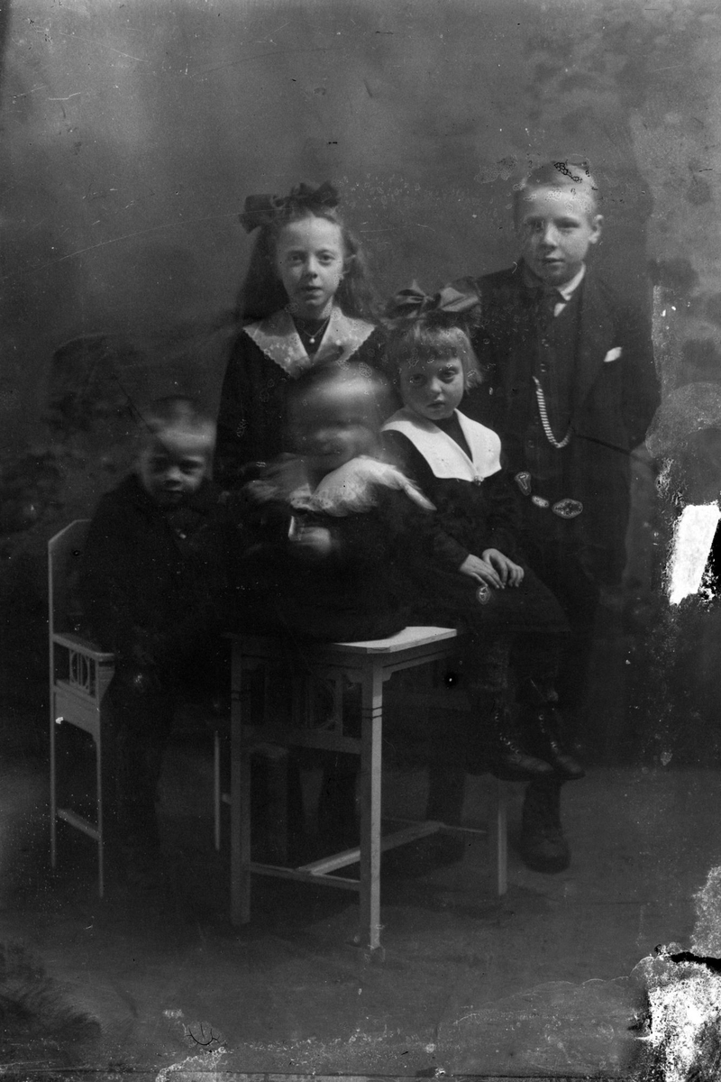 Studioportrett av fem barn ved et bord og en stol.