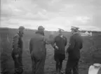 Militärflygare lämnar rapport till divisionschefen vid flygvapenövningen Västgötamanövern, 1931. Två flygare och två militärer ur Flygvapnet vid ett flygfält, flygplan i bakgrunden.