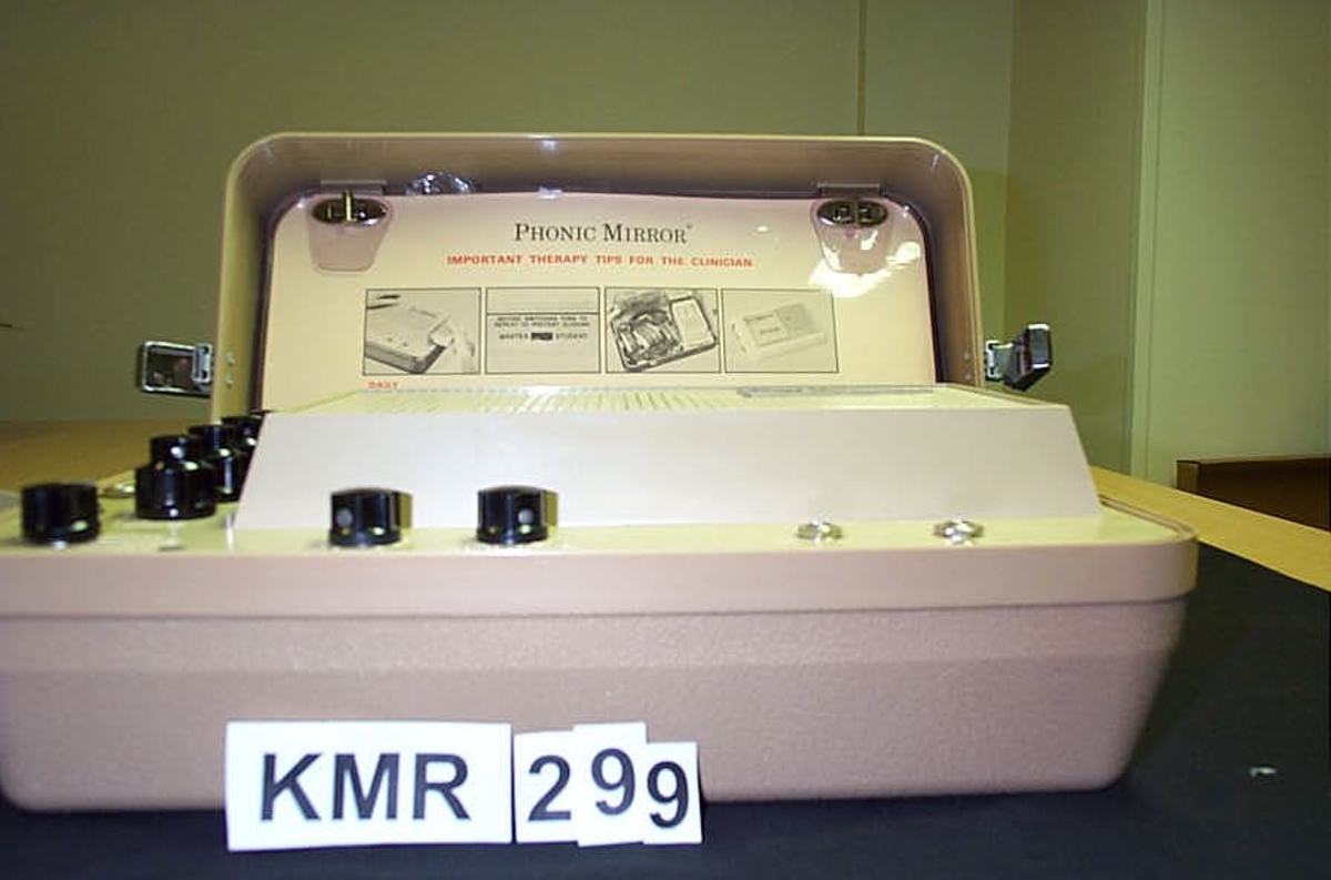 Talemaskin; koffert med utstyr, 9 deler, A hovedapparat, nederste del av kofferten, apparatet har 7 brune skruknotter, hvit ledning, B koffertens lokk som inneholder, C-D mikrofoner, E-F-G- kassetter, H øresett til lytting (høretelefon) I bruksanvisning alle deler pakket i plast