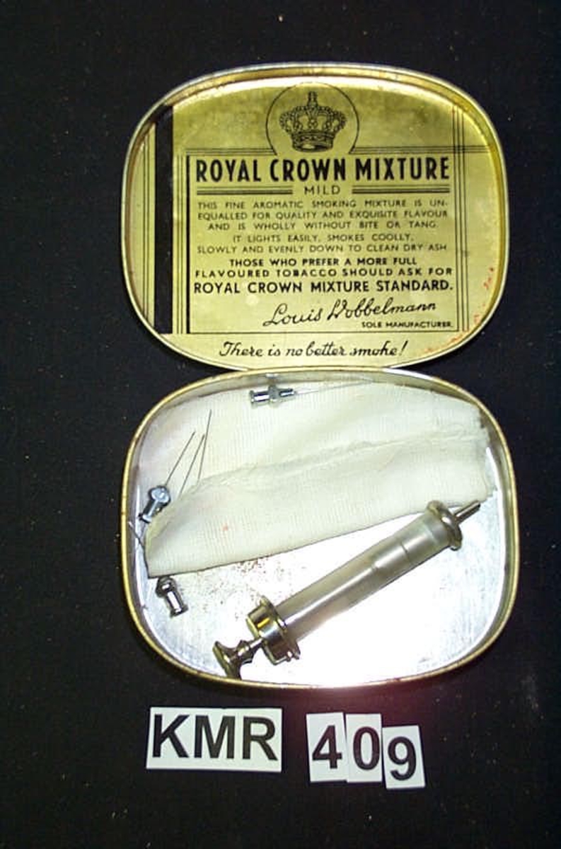 Royal Crown Mixture Manufactured by Louis Dobbelmann Rotterdam Holland. inni esken ligger, på et stk gas stoff, en sprøyte og 5 sprøytespisser. 