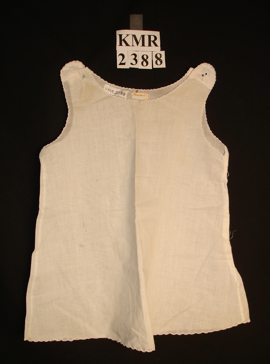 Liv, undertrøye til barn i tynn cambric. Tungekantet rundt ermer, hals og nedre del. A-formet fasong. Knepping på skuldrene.