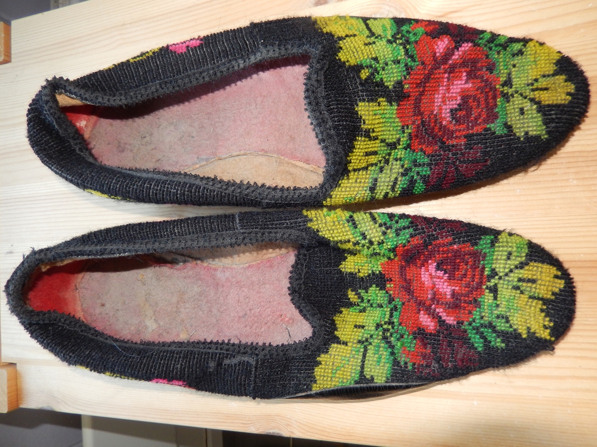 Tøfler, med brodert blomstermotiv på svart bunn. Motivet er brodert i rosa, rødt og ulike  grønnfarger.De er formet slik at de ligner en smekkefasong. 
Størrelse 43. Preget under LB.