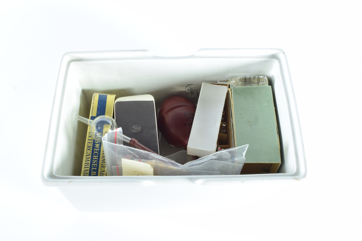 Skrin med lokk i hvit porselen. Skrinet inneholder diverse gjenstander brukt i apotekvirksomhet.

Skrinnet inneholder:

1 grønn eske med "Sterilpakning for kanyler". I esken ligger det 13 små rør i glass og 1 i plast.

1 hvit eske med 8 ampuller med Dolormin til injeksjon.

2 uåpnede pakker med sprøyter, produsert i Tyskland. Eskene er dekorert med et blått kors på en gullfarget bakgrunn og en logo som viser et hus og bostaven H.

2 kvadratiske metallbokser med sprøyter. På lokket til en av boksene er det en logo som viser et hus og bokstaven H.

1 pose med seks munnstykker til nesespylere.

1 lite knivblad med tager og bokstavene A L.

1 pose med flere små stålrør med et lite dråpeformet "håndtak" i en ende.

1 liten pumpe i rød gummi.