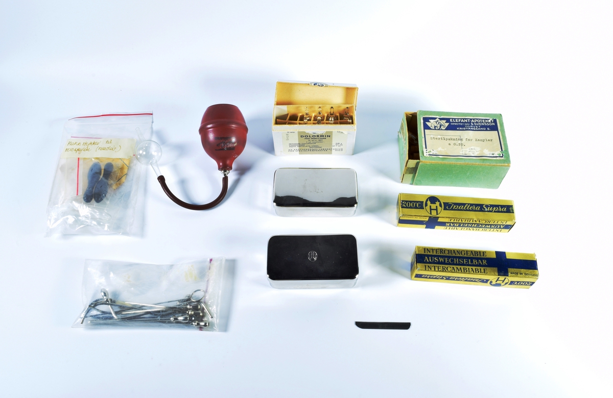 Skrin med lokk i hvit porselen. Skrinet inneholder diverse gjenstander brukt i apotekvirksomhet.

Skrinnet inneholder:

1 grønn eske med "Sterilpakning for kanyler". I esken ligger det 13 små rør i glass og 1 i plast.

1 hvit eske med 8 ampuller med Dolormin til injeksjon.

2 uåpnede pakker med sprøyter, produsert i Tyskland. Eskene er dekorert med et blått kors på en gullfarget bakgrunn og en logo som viser et hus og bostaven H.

2 kvadratiske metallbokser med sprøyter. På lokket til en av boksene er det en logo som viser et hus og bokstaven H.

1 pose med seks munnstykker til nesespylere.

1 lite knivblad med tager og bokstavene A L.

1 pose med flere små stålrør med et lite dråpeformet "håndtak" i en ende.

1 liten pumpe i rød gummi.